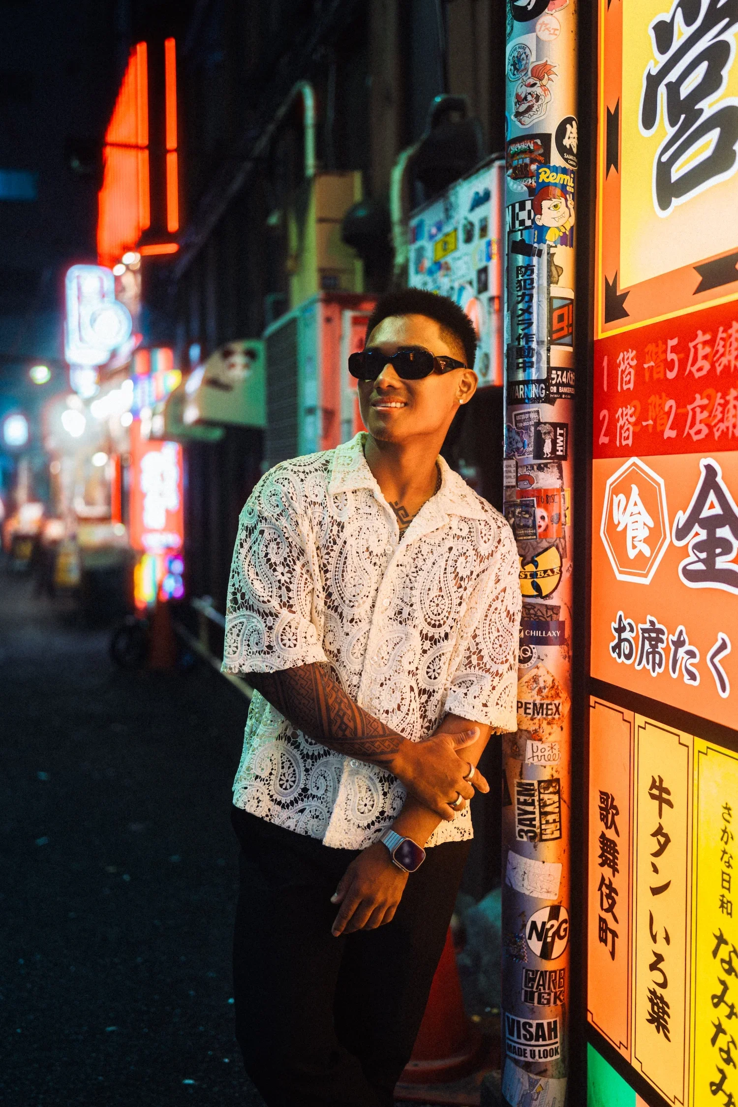 Man posing beside colorful neon signs during a professional Tokyo street style photoshoot