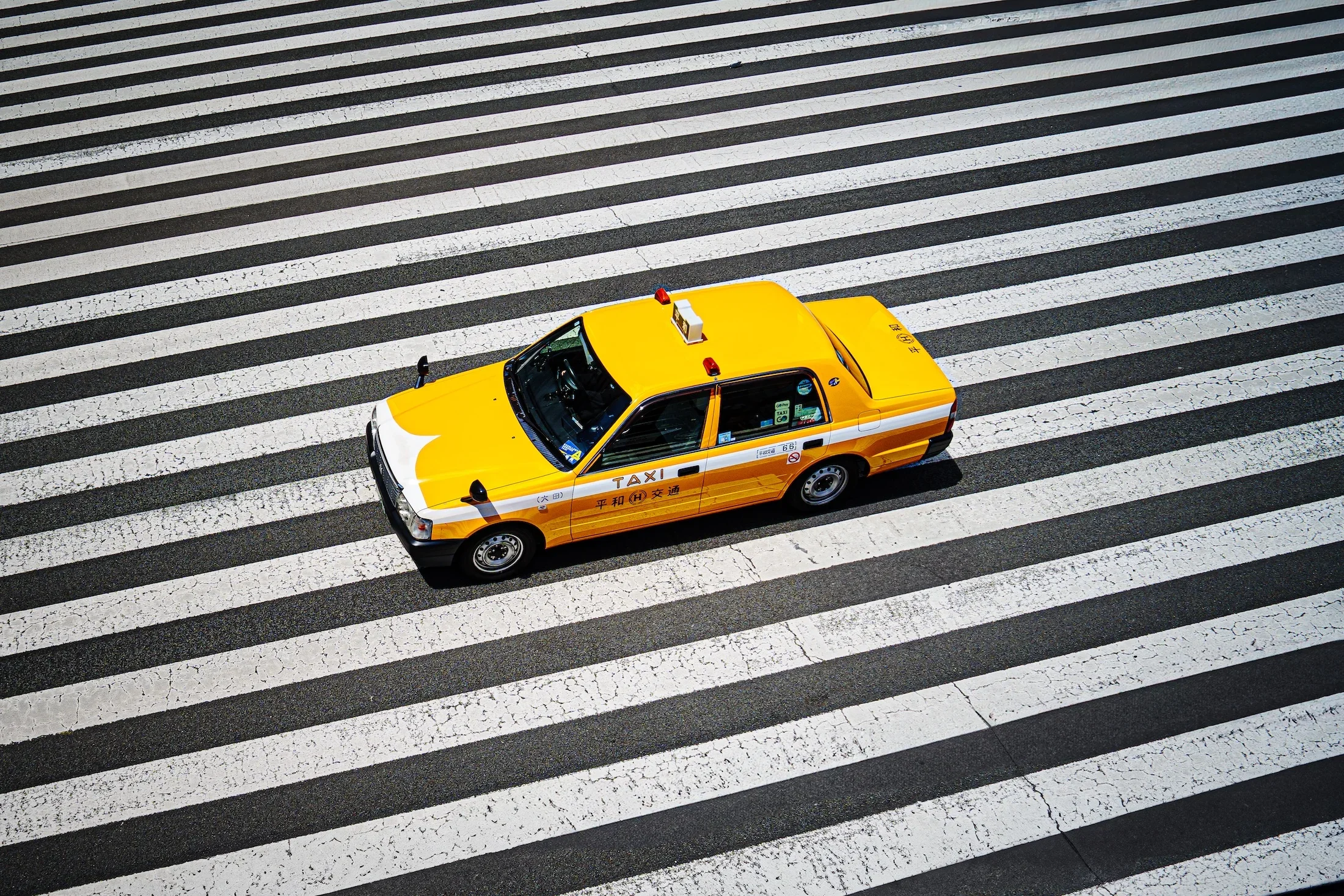 A yellow taxi cab crossing a striped crosswalk on a city street.