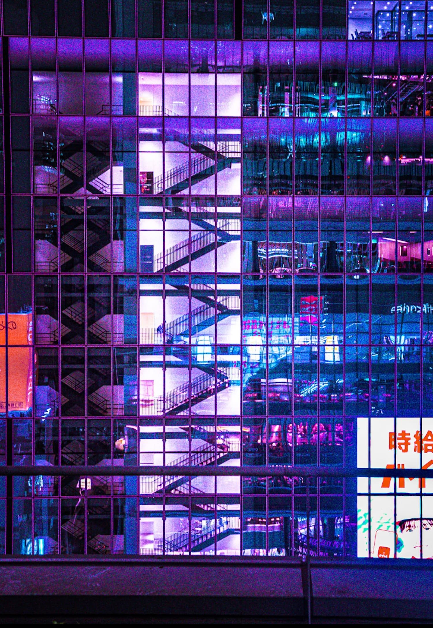 Night view of a multi-story parking garage reflected on a glass building with neon purple and blue lights taken on the Tokyo Cyberpunk Street photography workshop in Shibuya.