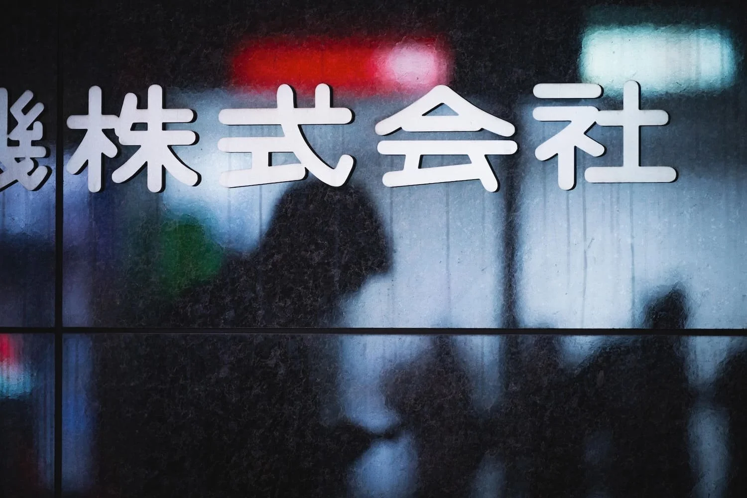 A foggy, wet glass wall with Japanese characters on it and a person holding an umbrella in the background shot during a Ginza Tokyo street photography workshop.