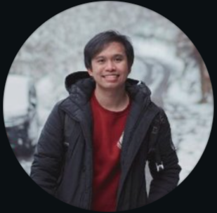 A young man smiling outdoors with a snowy background, wearing a black jacket and red shirt.
