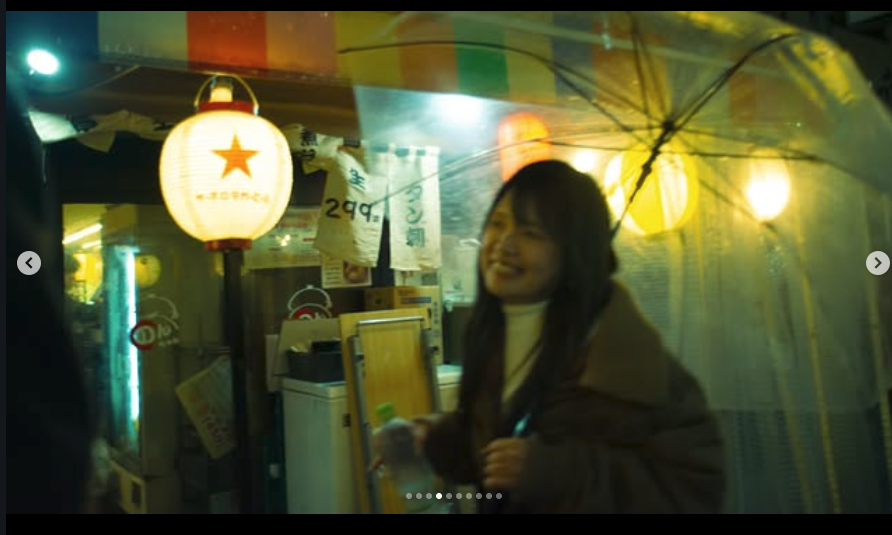 A smiling woman holding an umbrella inside a decorated indoor space with Japanese lanterns and banners.