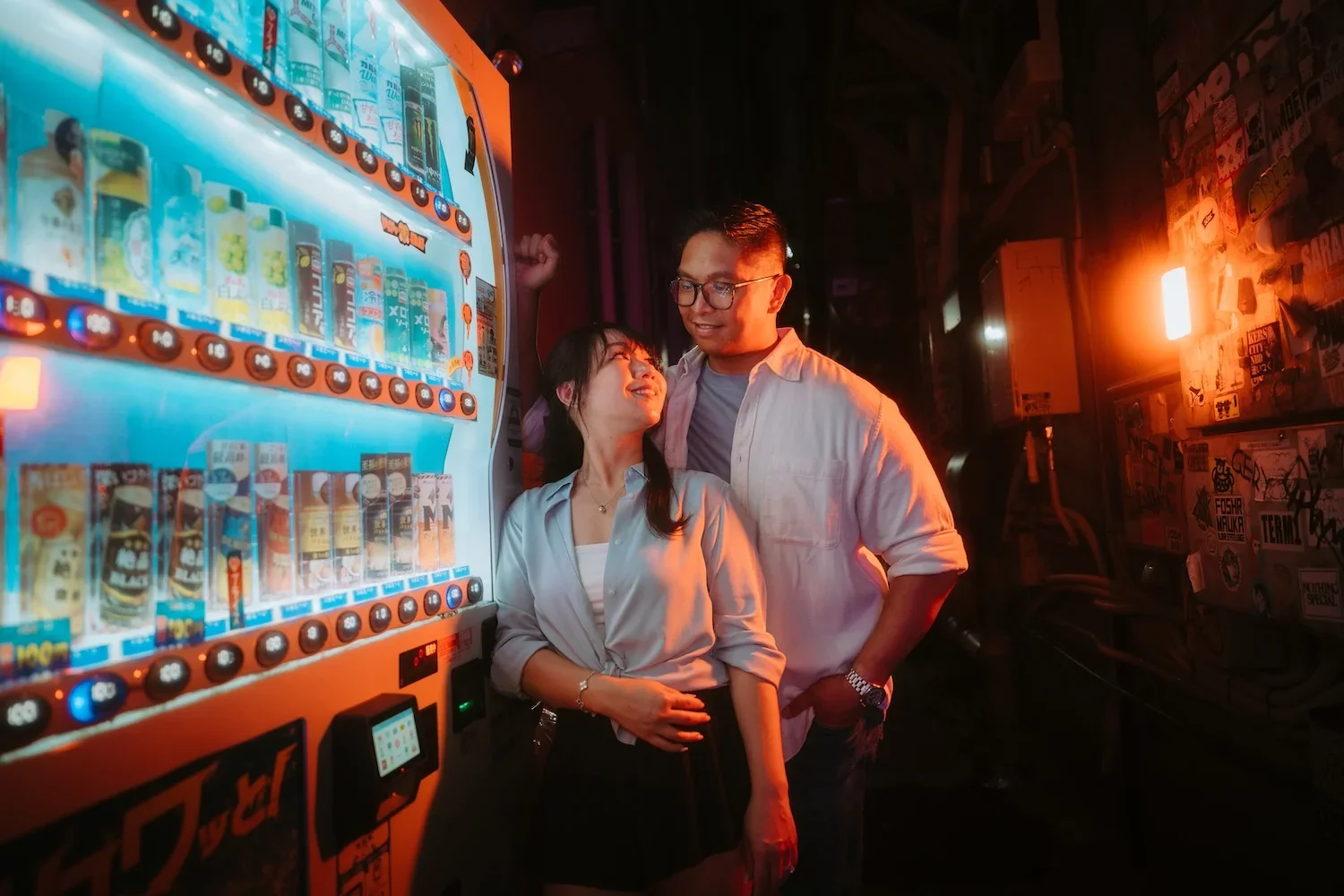 Couple sharing a playful moment beside glowing vending machines during a Tokyo night photoshoot with Tokyo photographer Deniz Demir