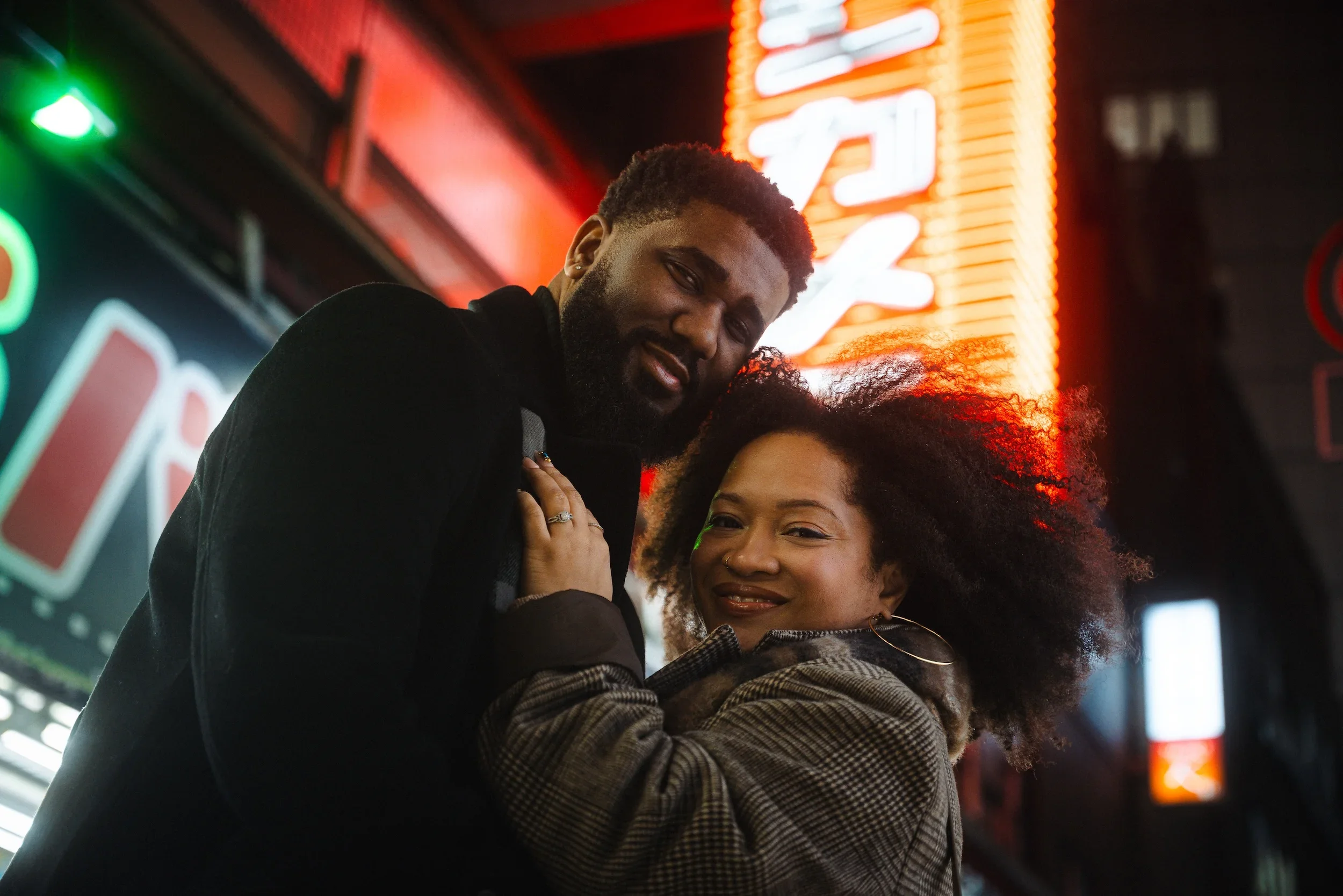 Couple embracing beneath colorful neon signs during a professional Tokyo night photoshoot