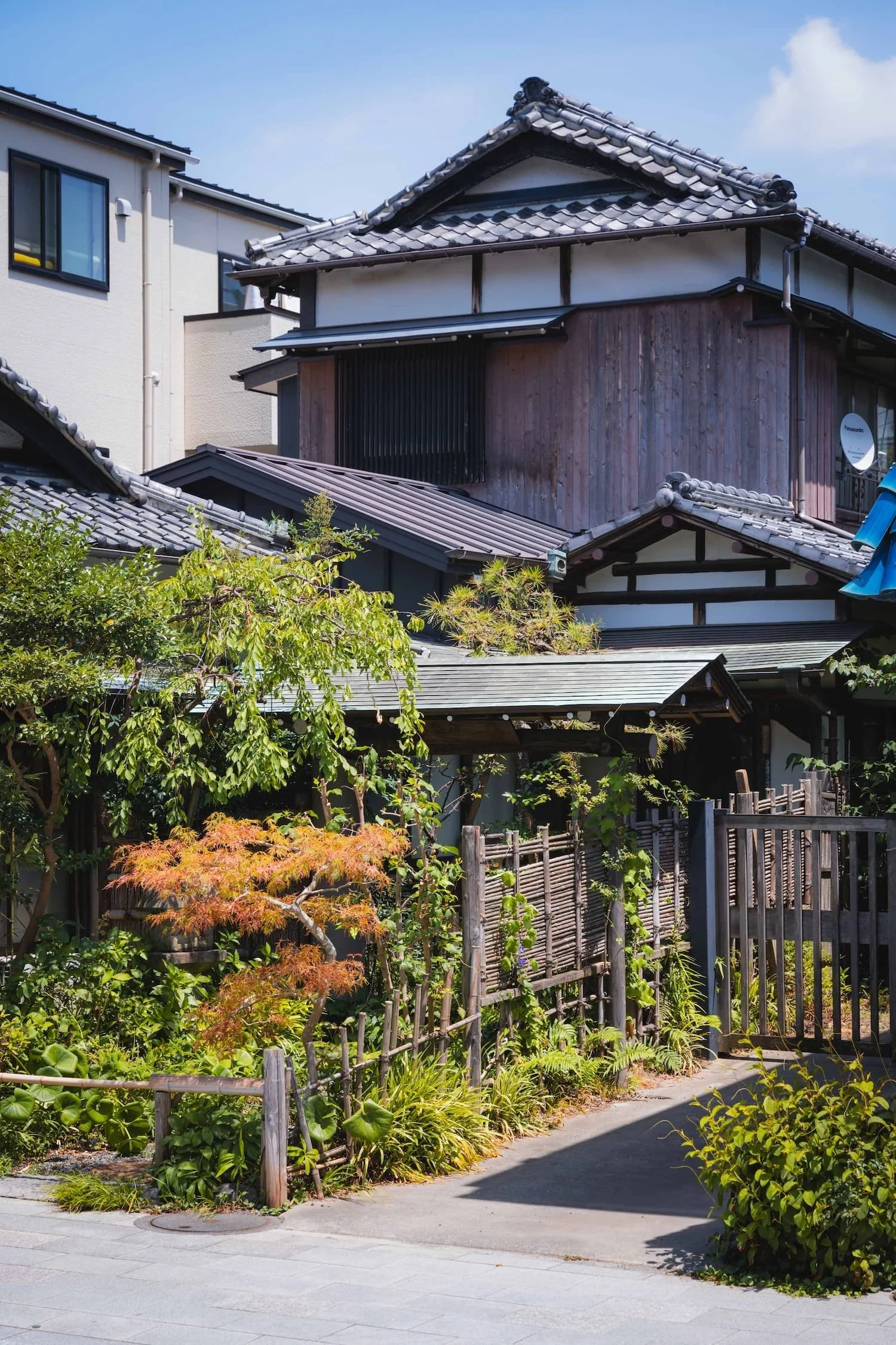 Traditional Japanese house with tiled roof, wooden exterior, surrounded by lush greenery and a small garden.