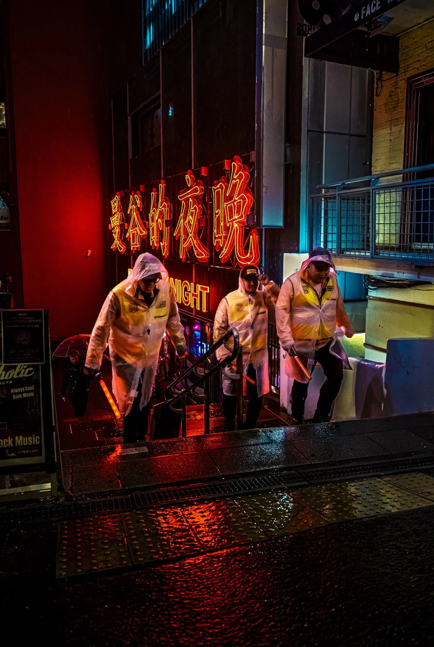 Nighttime scene outside a bar or club with a neon sign in Chinese characters and the word 'NIGHT' in English. Three people wearing raincoats and holding illuminated objects walk across a wet sidewalk.