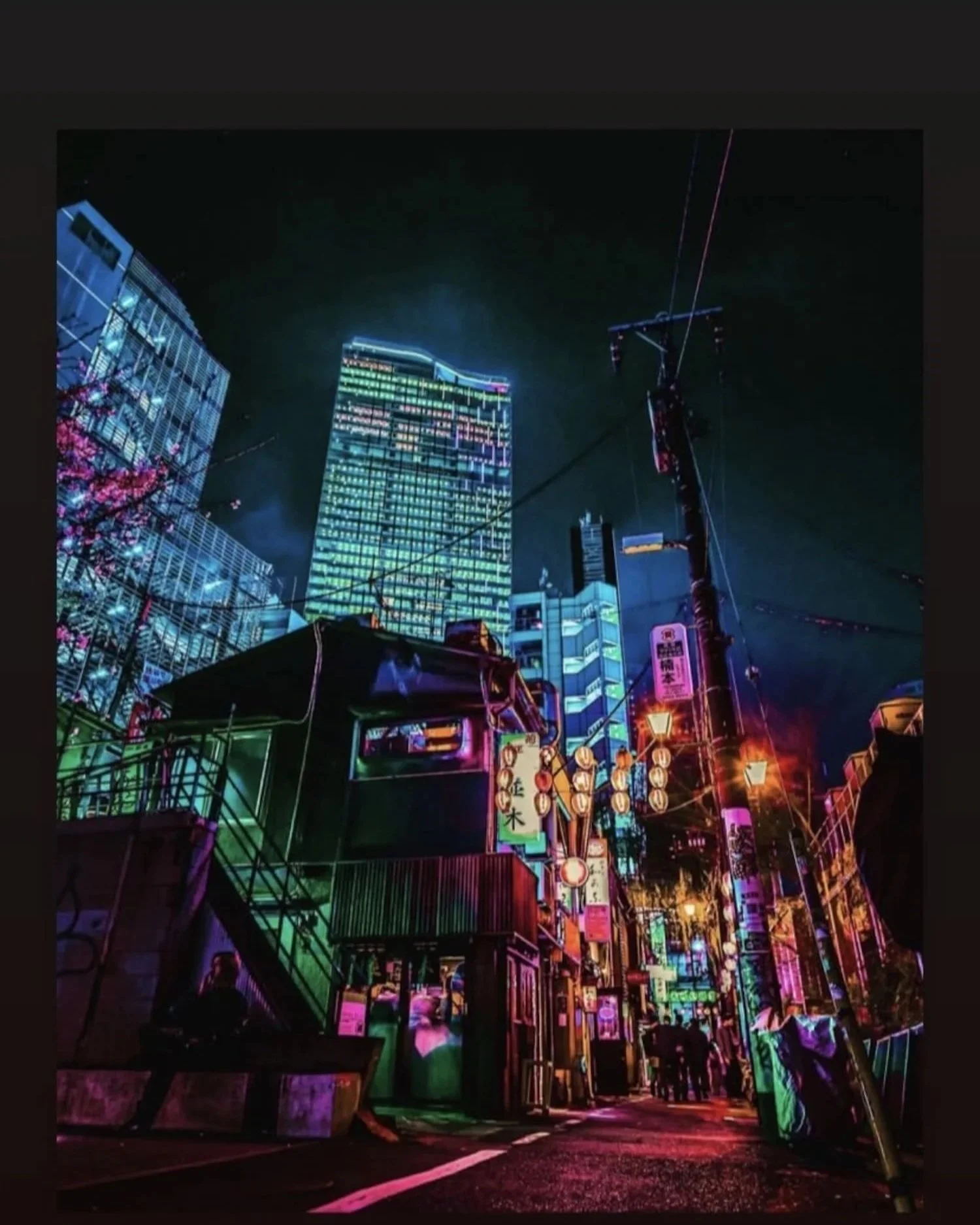 Night view of illuminated city street with colorful neon signs, tall buildings, and street lanterns.