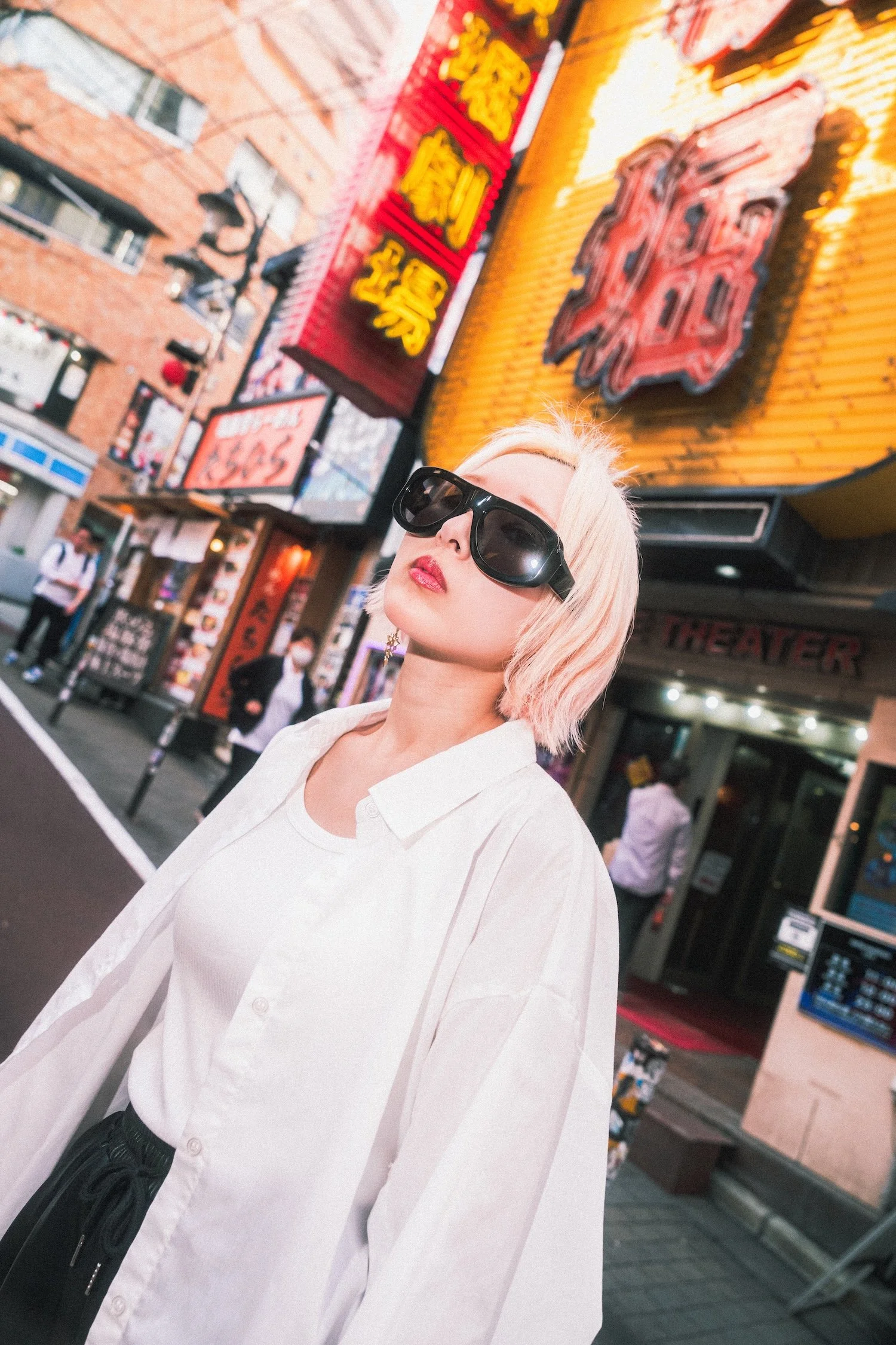 Street fashion campaign for Vasuma Eyewear in Tokyo, showing a model wearing oversized sunglasses against illuminated restaurant signs and the vibrant neons of Shibuya during the daytime.