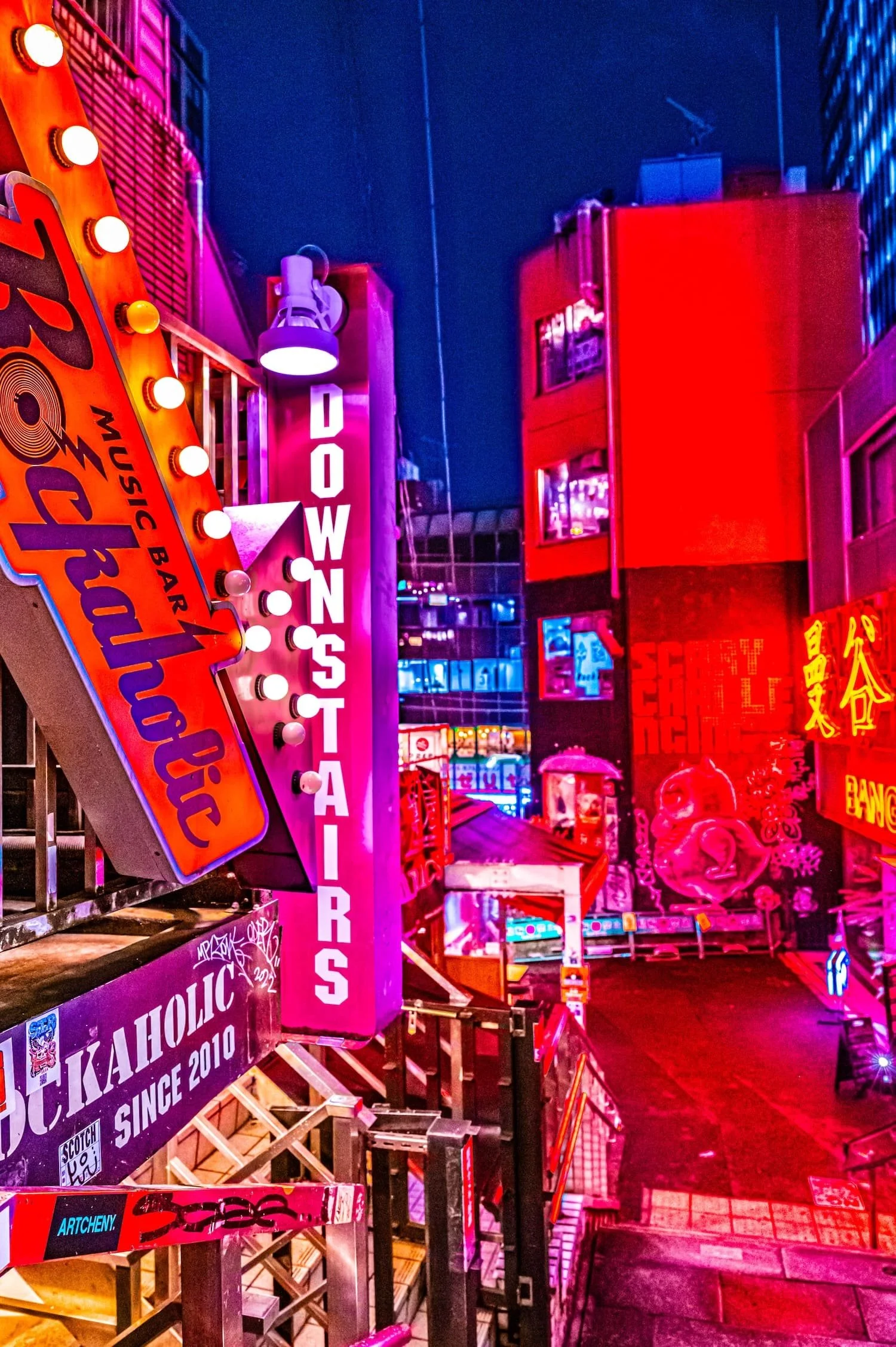 Night view of brightly lit neon signs and buildings in a city with vibrant pink, red, and blue lights