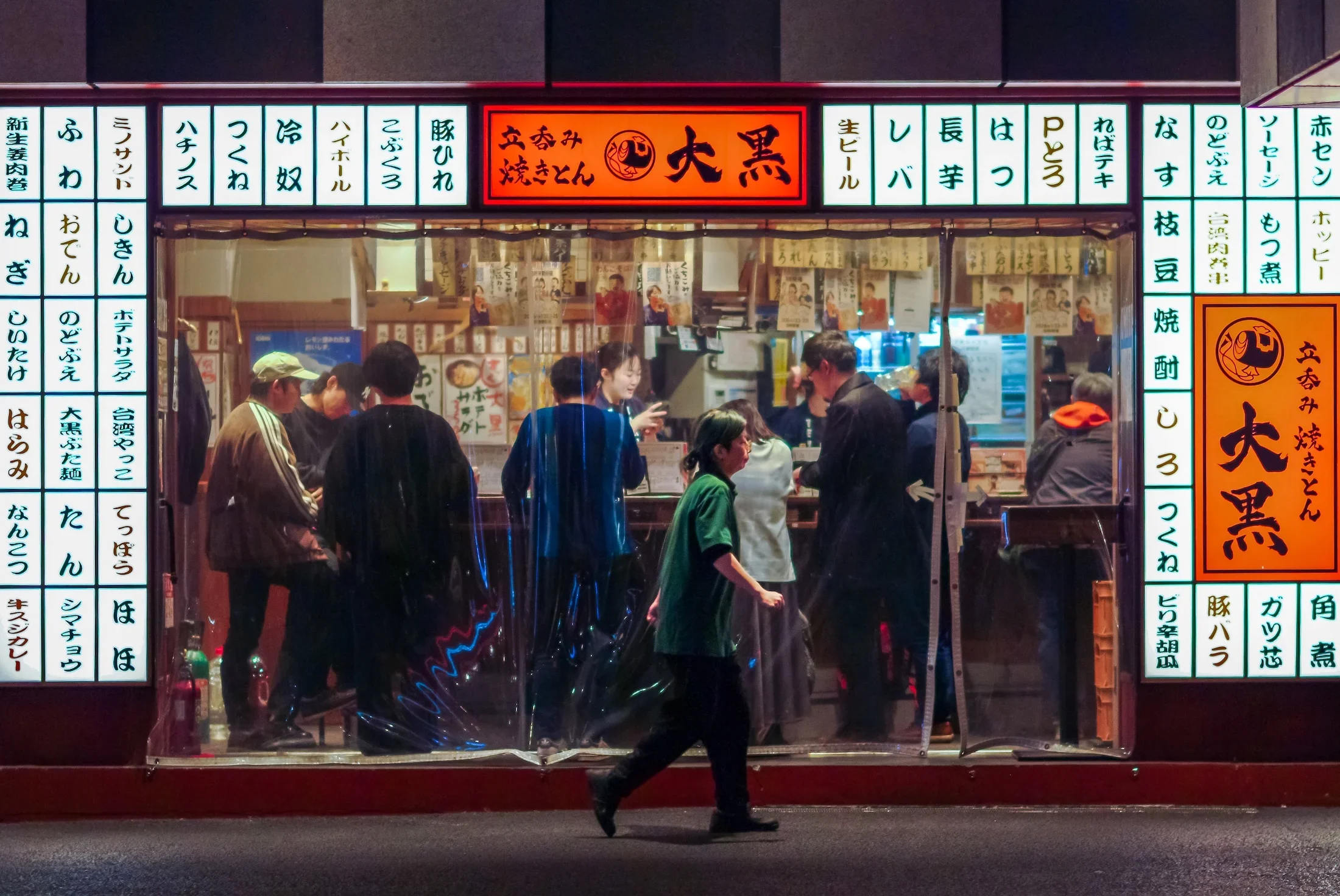 People standing outside a Japanese restaurant with illuminated menu signs in Japanese characters at night.