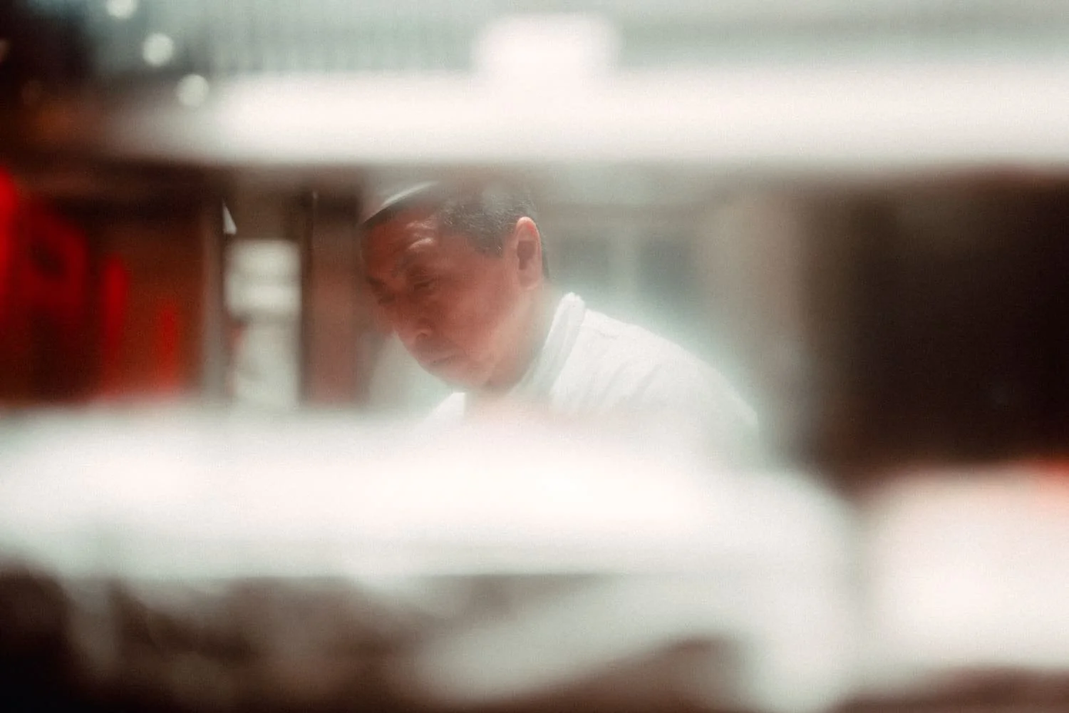 A person wearing a white shirt, seen through a blurred and partially obstructed view. Shot by Tokyo photographer.Deniz Demir during a Tekumi street photography workshop called Tokyo Izakayas.