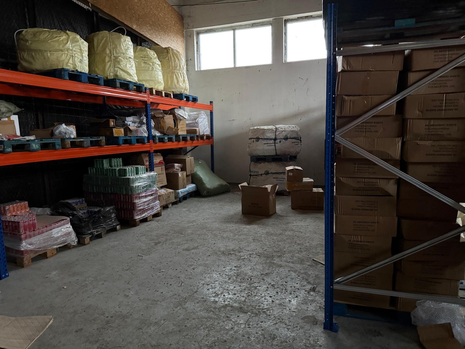 Storage room with metal shelving holding large bags, boxes, and supplies, near a window with natural light.