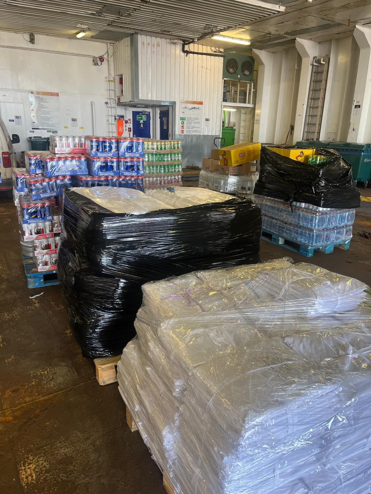 Pallets of canned and bottled beverages, including water and soda, stacked in an industrial warehouse.
