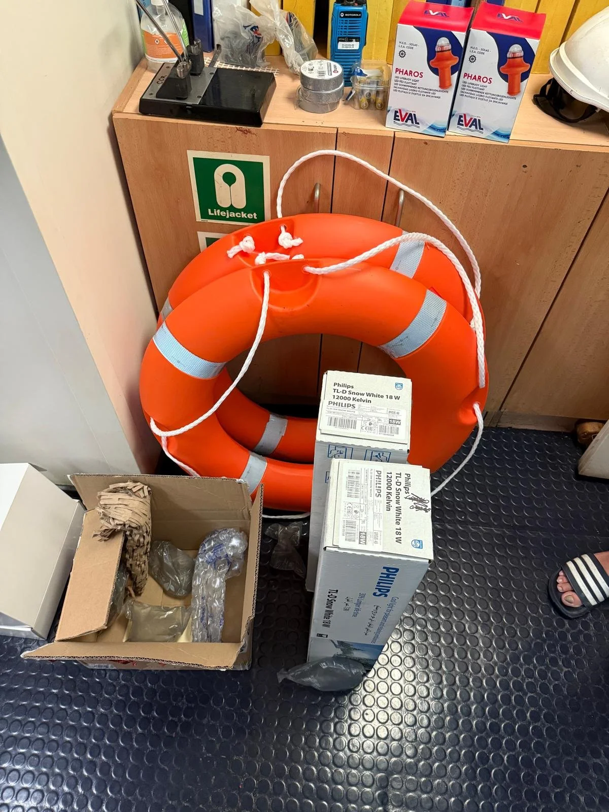 Stacked orange life jackets leaning against a wooden cabinet with boxes of LED snow lights and other supplies on top.