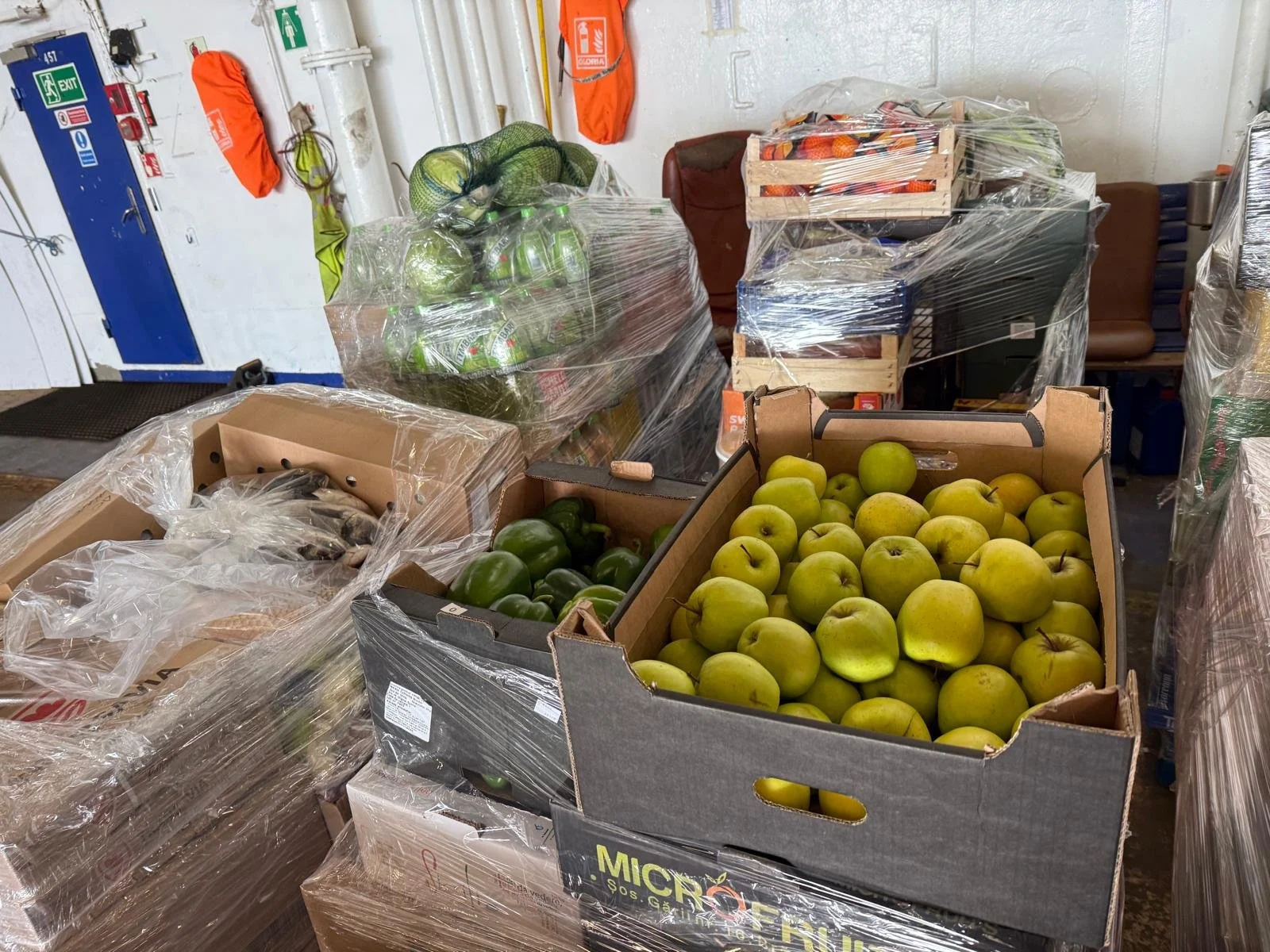Boxes of green apples and other produce wrapped in plastic in a storage or warehouse area.