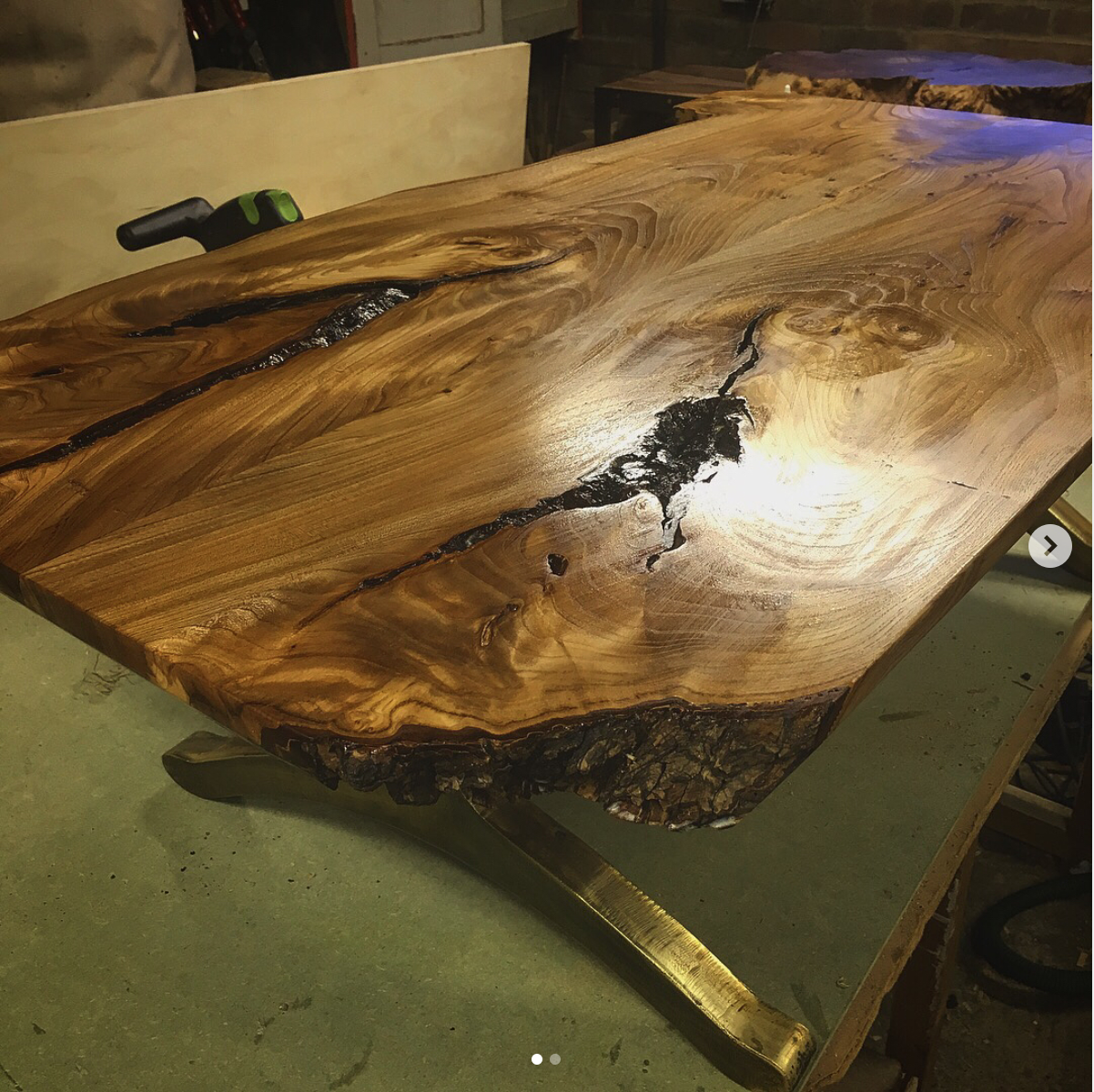 Close-up of a wooden table with a natural live edge and dark resin-filled cracks, showcasing intricate wood grain patterns.