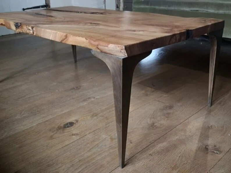 A wooden table with a live edge and metal legs on a wooden floor.
