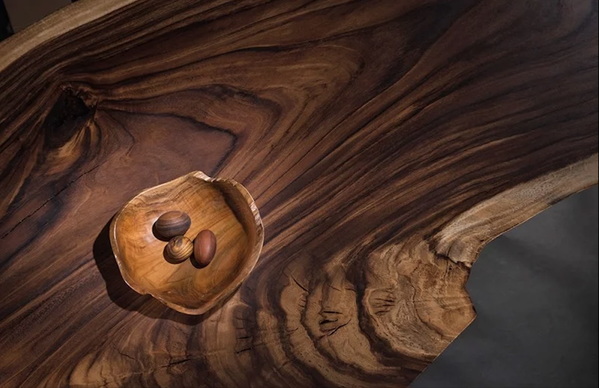 Close-up of a natural wood surface with three small wooden eggs inside a carved wooden bowl.