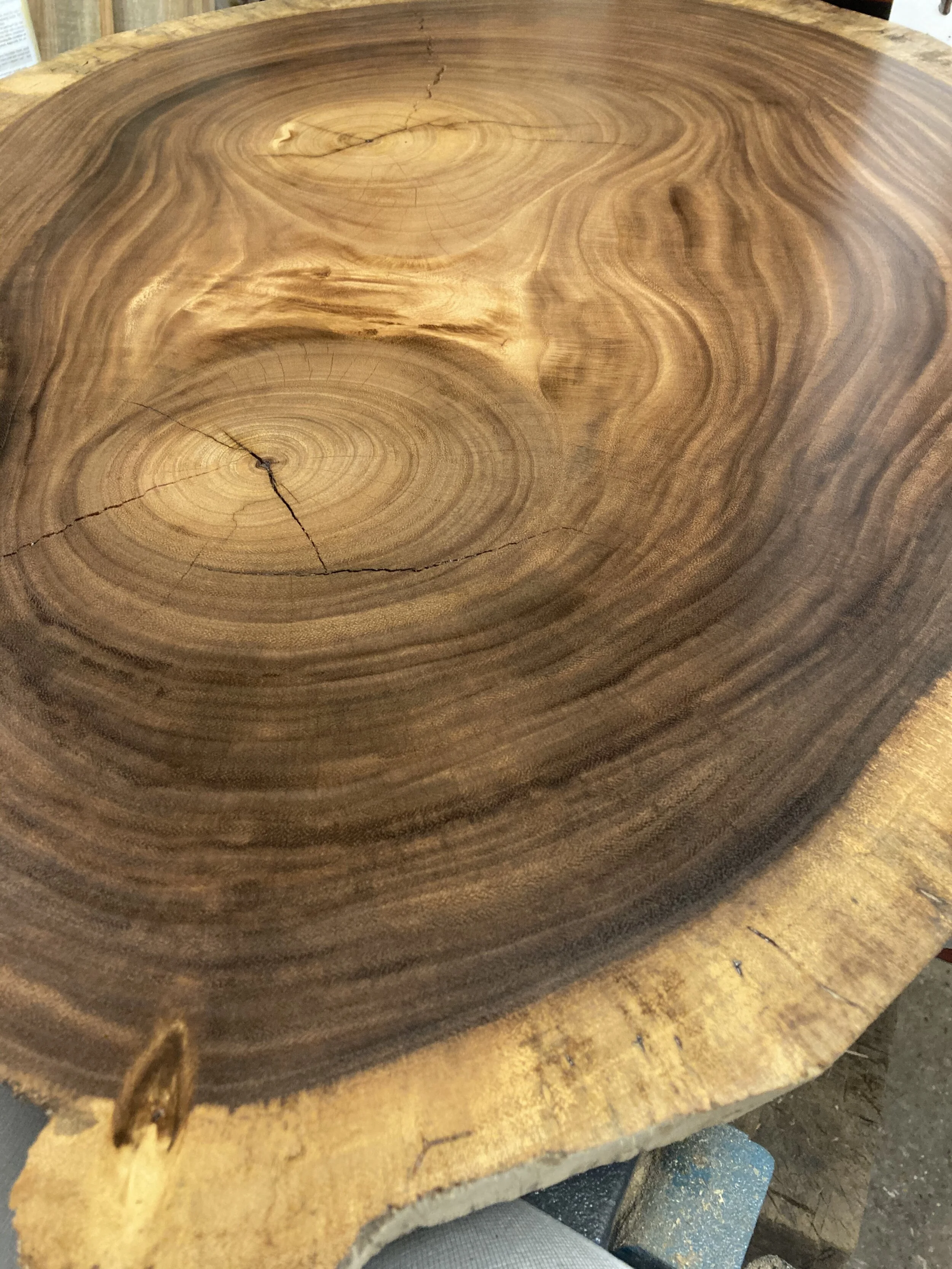 Close-up of a round wooden slab with visible tree rings and natural cracks, used as a tabletop surface.