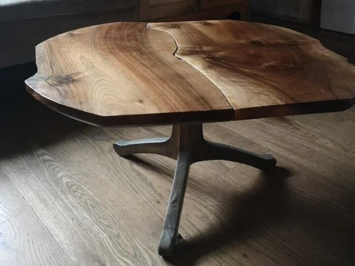 A wooden table with a thick, natural-cut wood top and a metal base on a wooden floor.