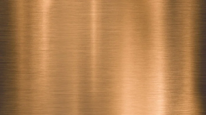 A close-up of a metallic surface with a smooth, brushed texture and a copper or bronze color.