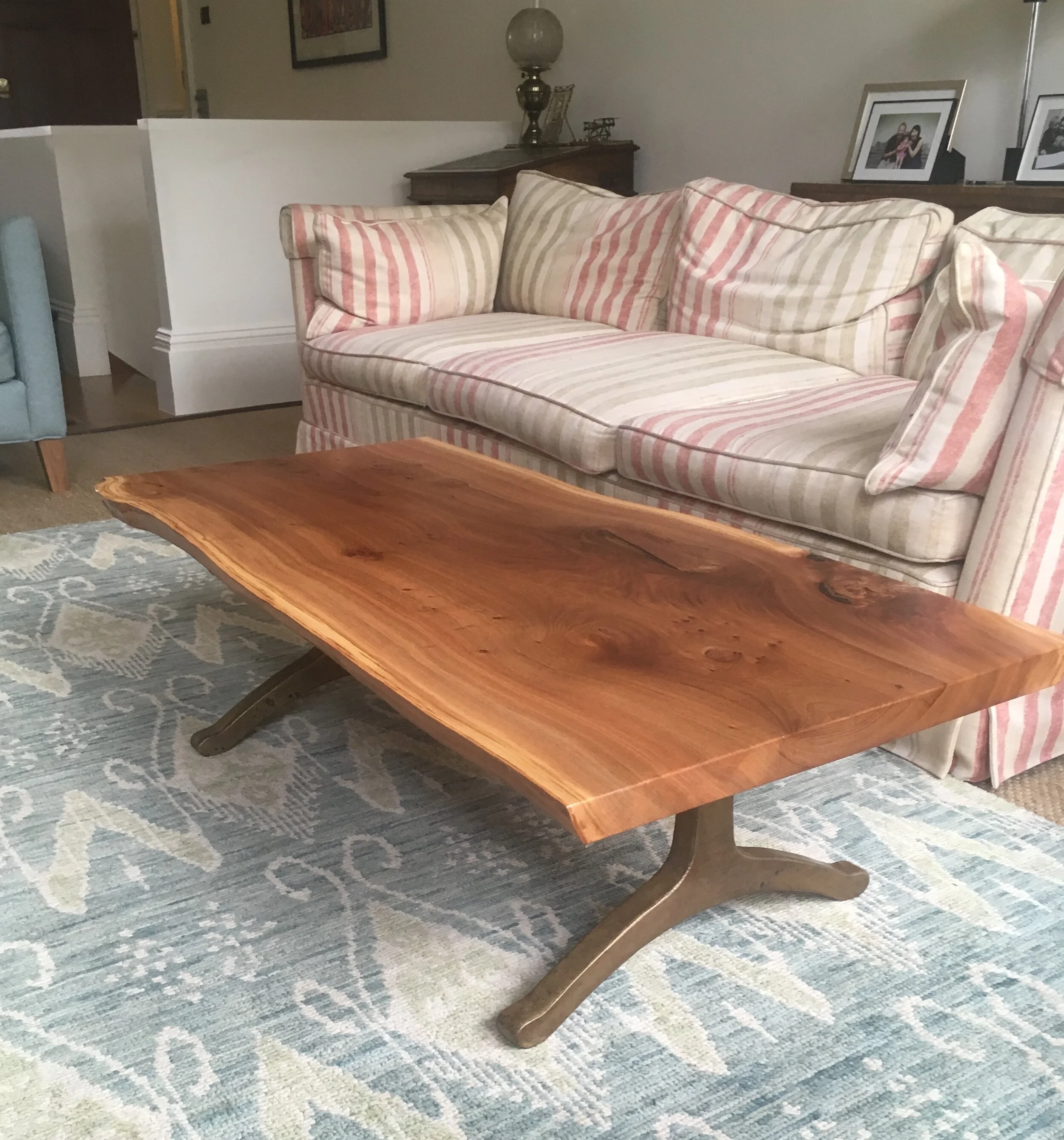 A wooden coffee table with curved legs on a light blue patterned rug in front of a striped sofa.