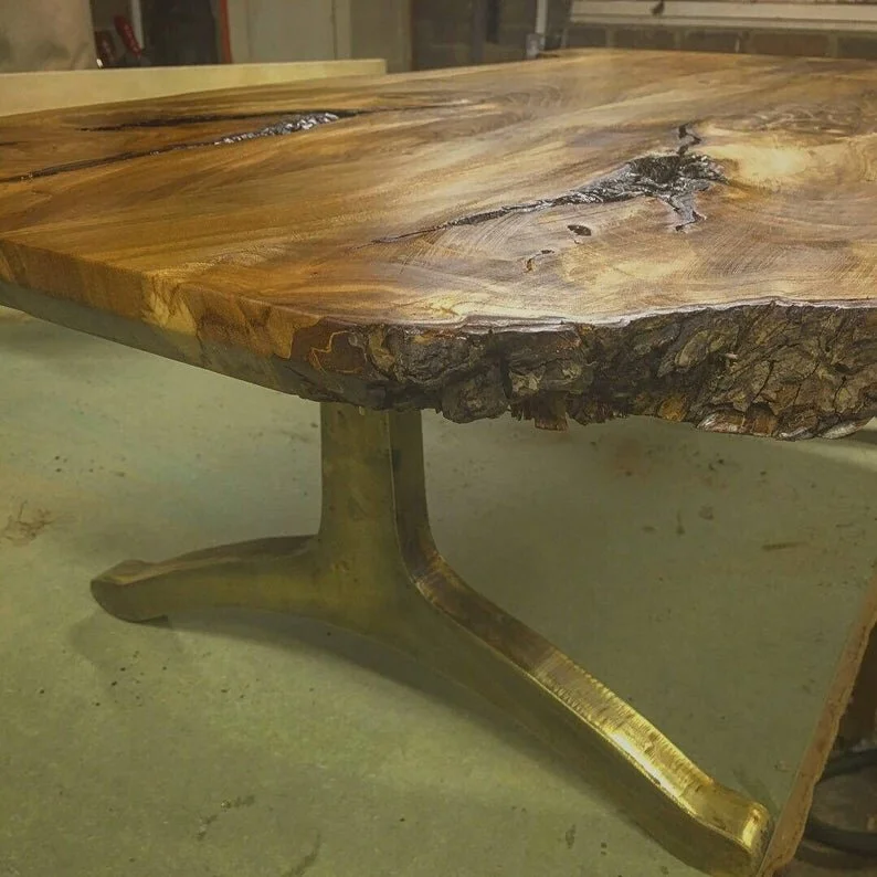 Close-up of a wooden table with a live edge, supported by a curved metal base.