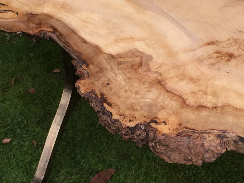 Close-up of a natural wood slab with a live edge, placed on green grass.