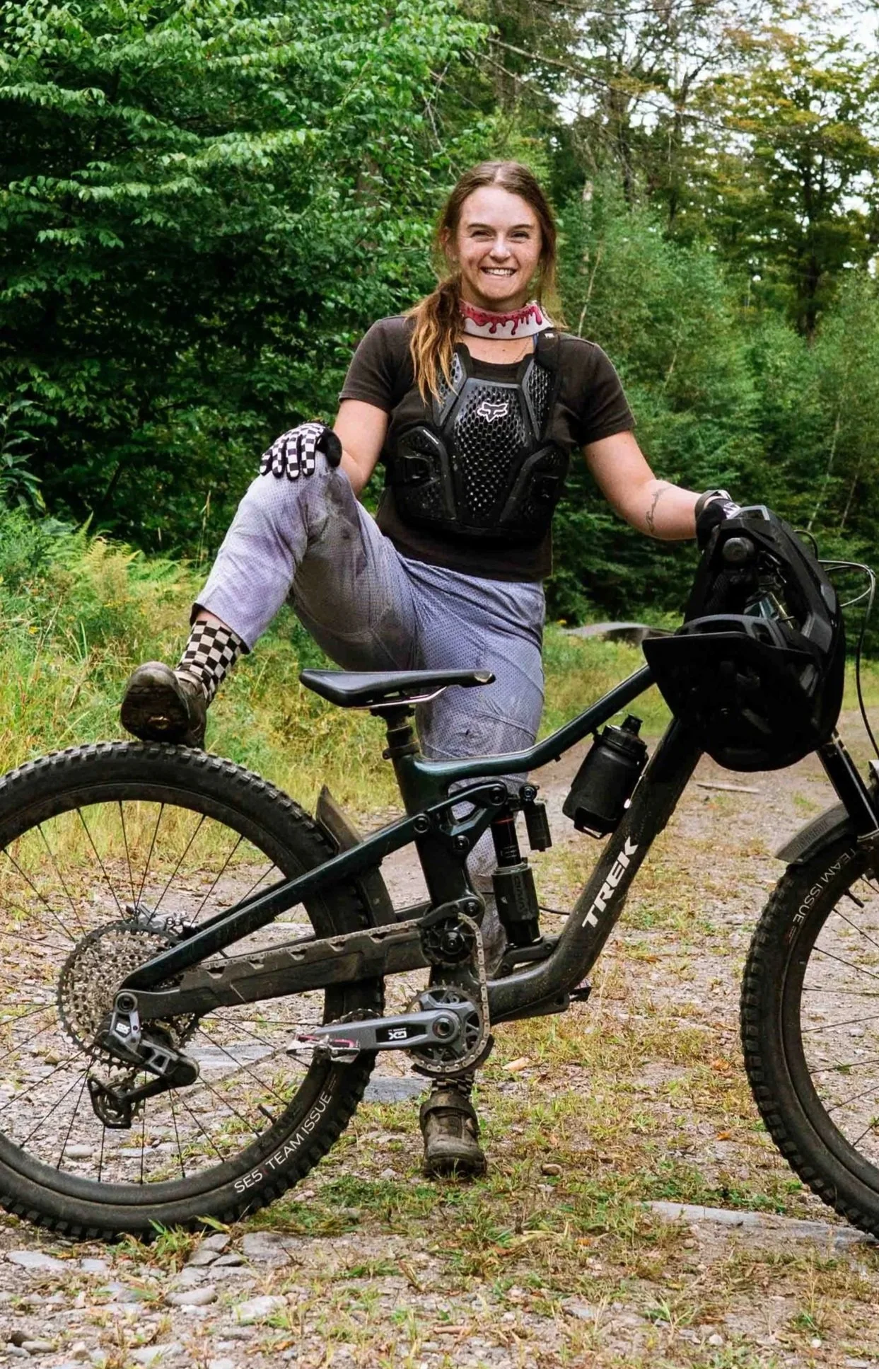Mountain Bike Coach for MTB Skills Factory, Lilly Driver stands with her mountain bike for a profile shot smiling with one foot on the rear tire