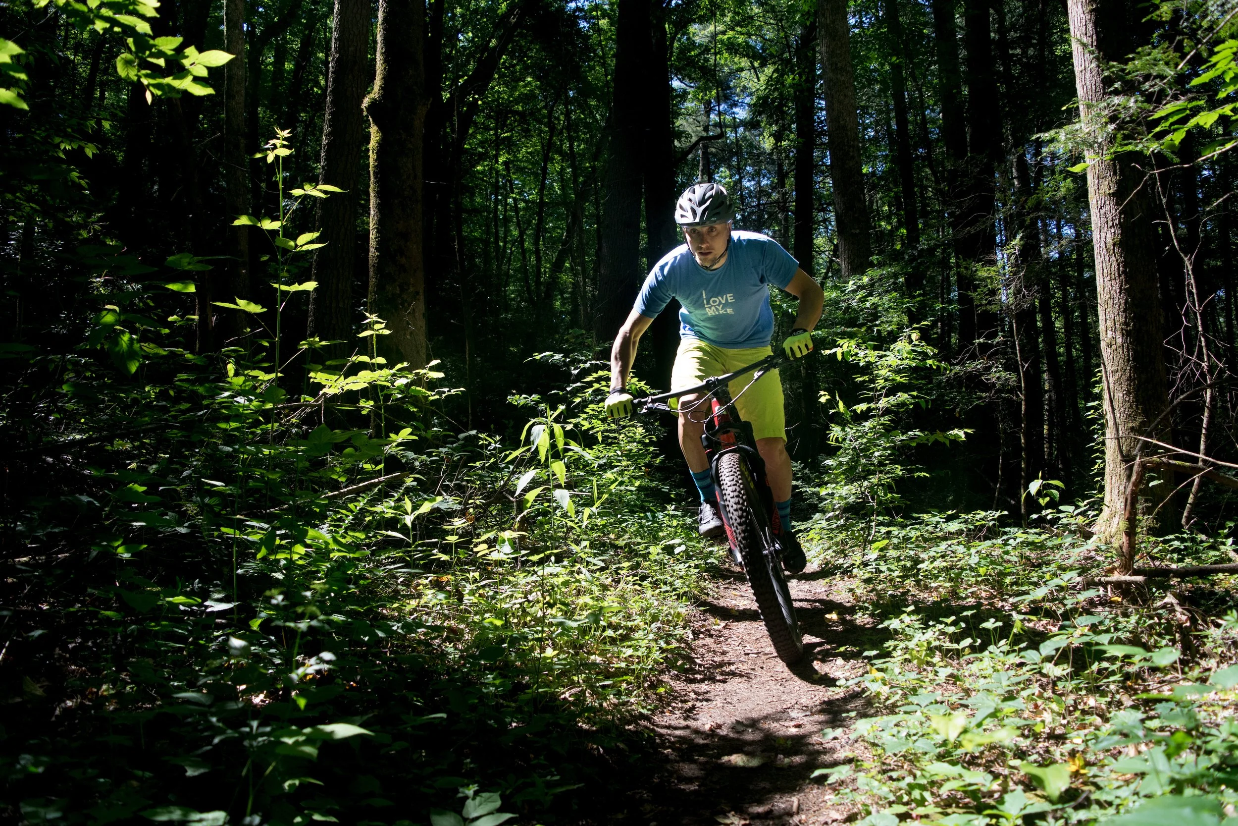 Mountain biker in pisgah stands up to accelerate across a smooth section of trail surrounded by green vegetation