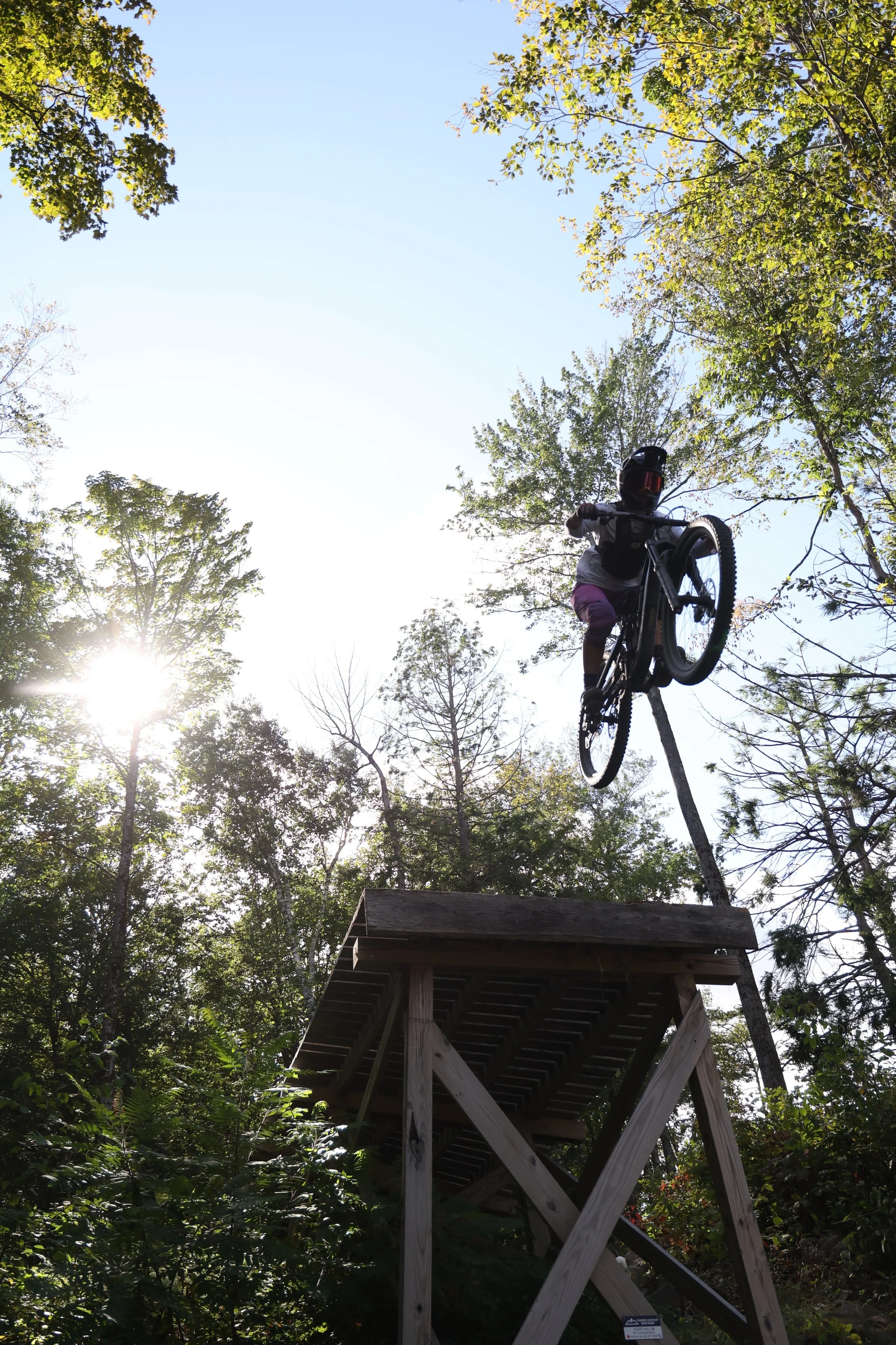 MTB Skills Factory Coach Lilly Driver rides an enormous drop on her mountain bike with the sun in the background
