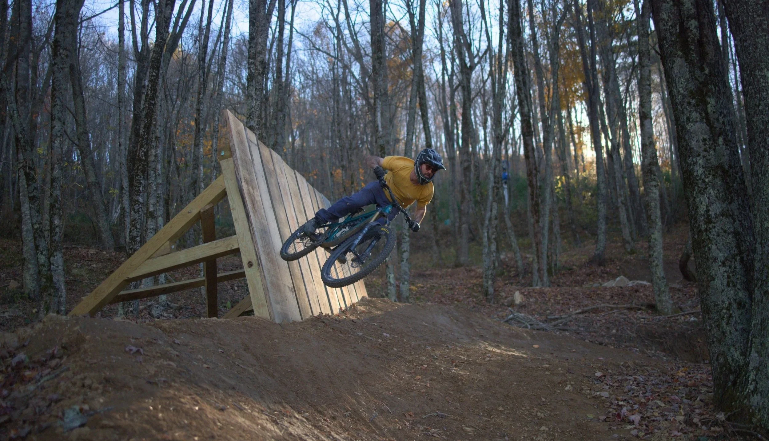 downhill mountain biker using wooden features to jump off in the waning evening fall light