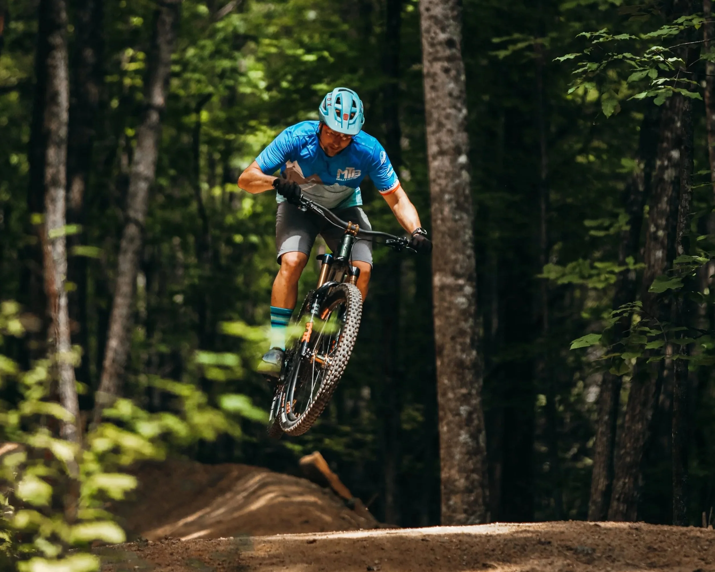 a mountain biker jumps a dirt roller on trail in the Old Fort Gateway Trail Region