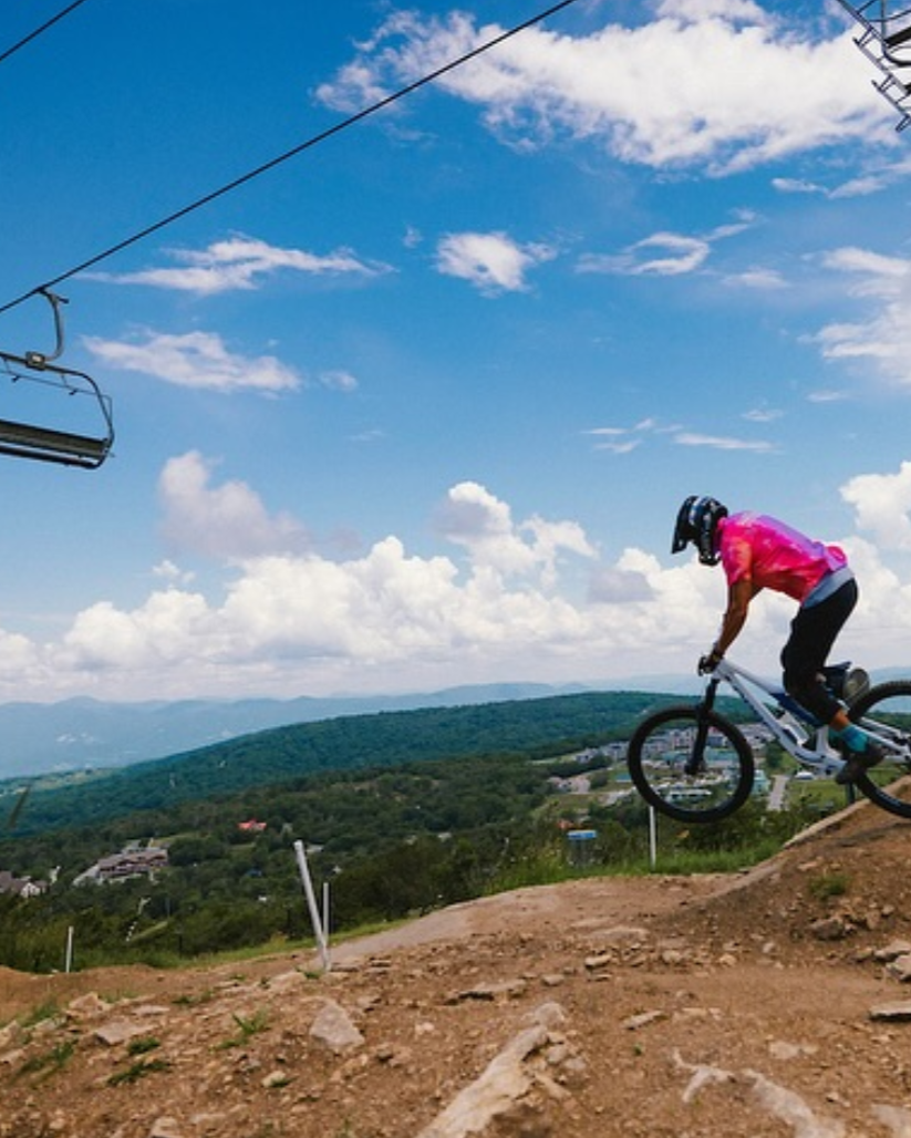 A mountain biker rides off a dirt jump under the chairlift at Beech Mountain Bike Park