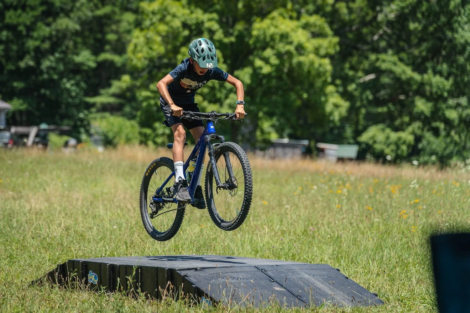 Young rider jumping his mountain bike on a ramp in a field. He looks to be having a blast!