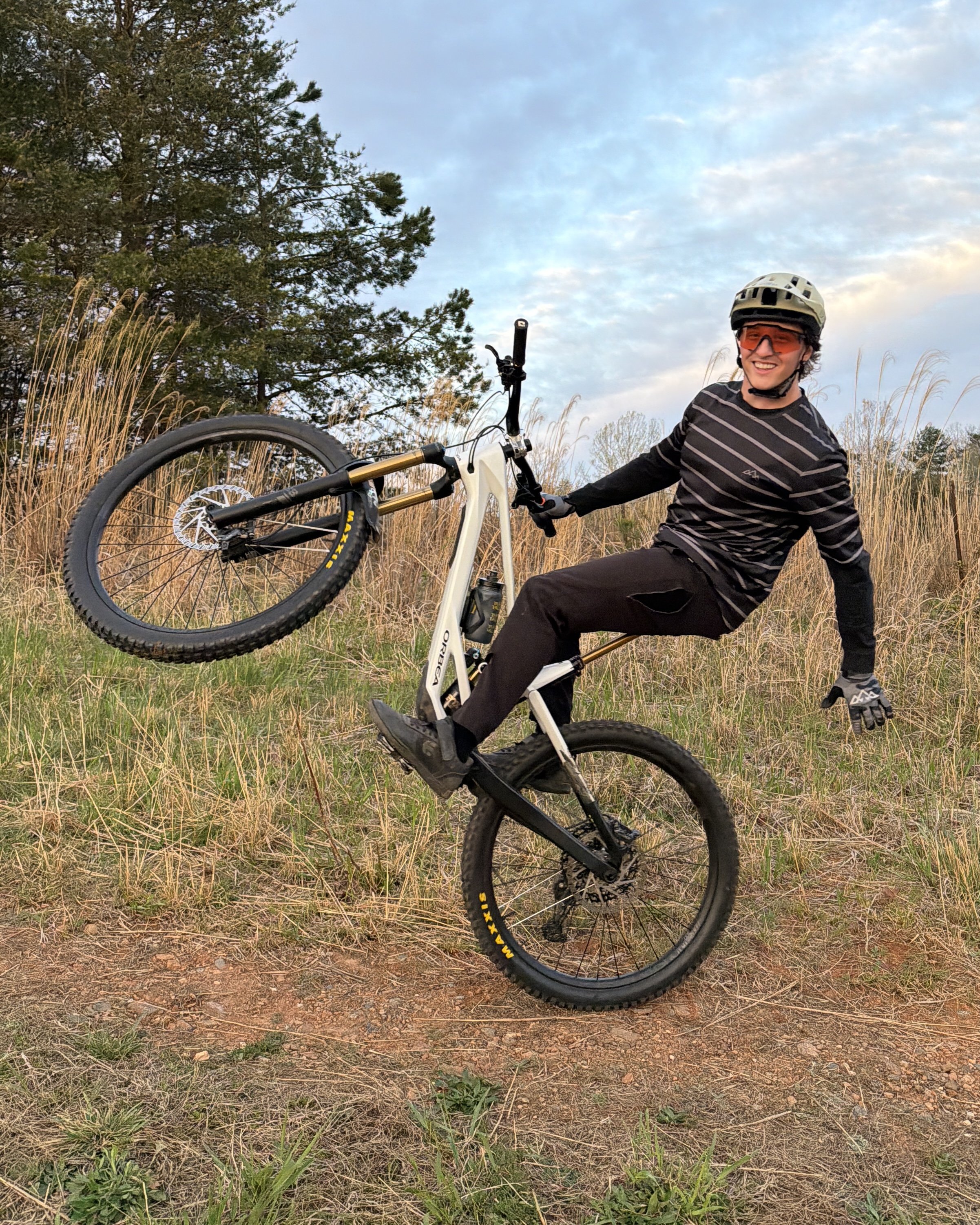 Mountain Bike Coach Allen Messersmith does a one handed wheelie while smiling at the camera
