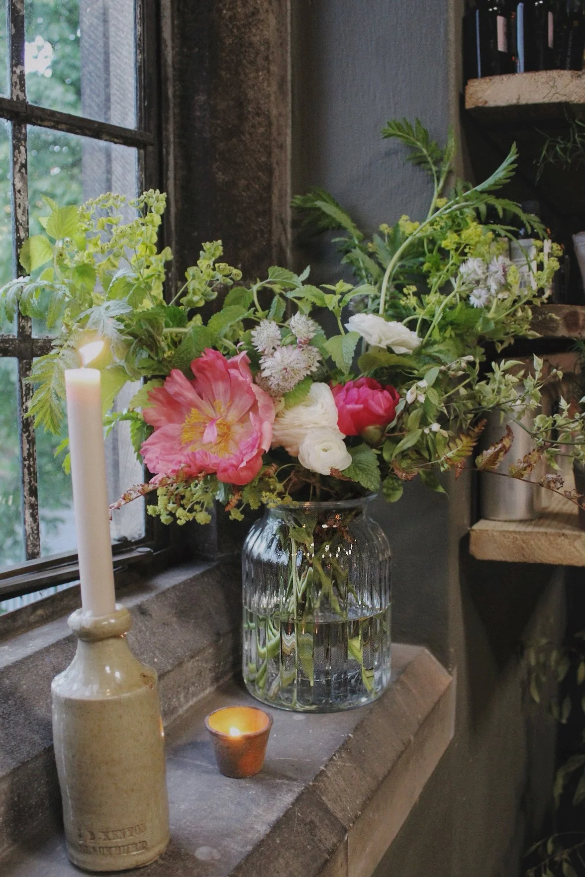 Large ribbed glass grand centrepiece filled with abundant seasonal flowers and foliage, styled with candles for a wedding table or feature display.