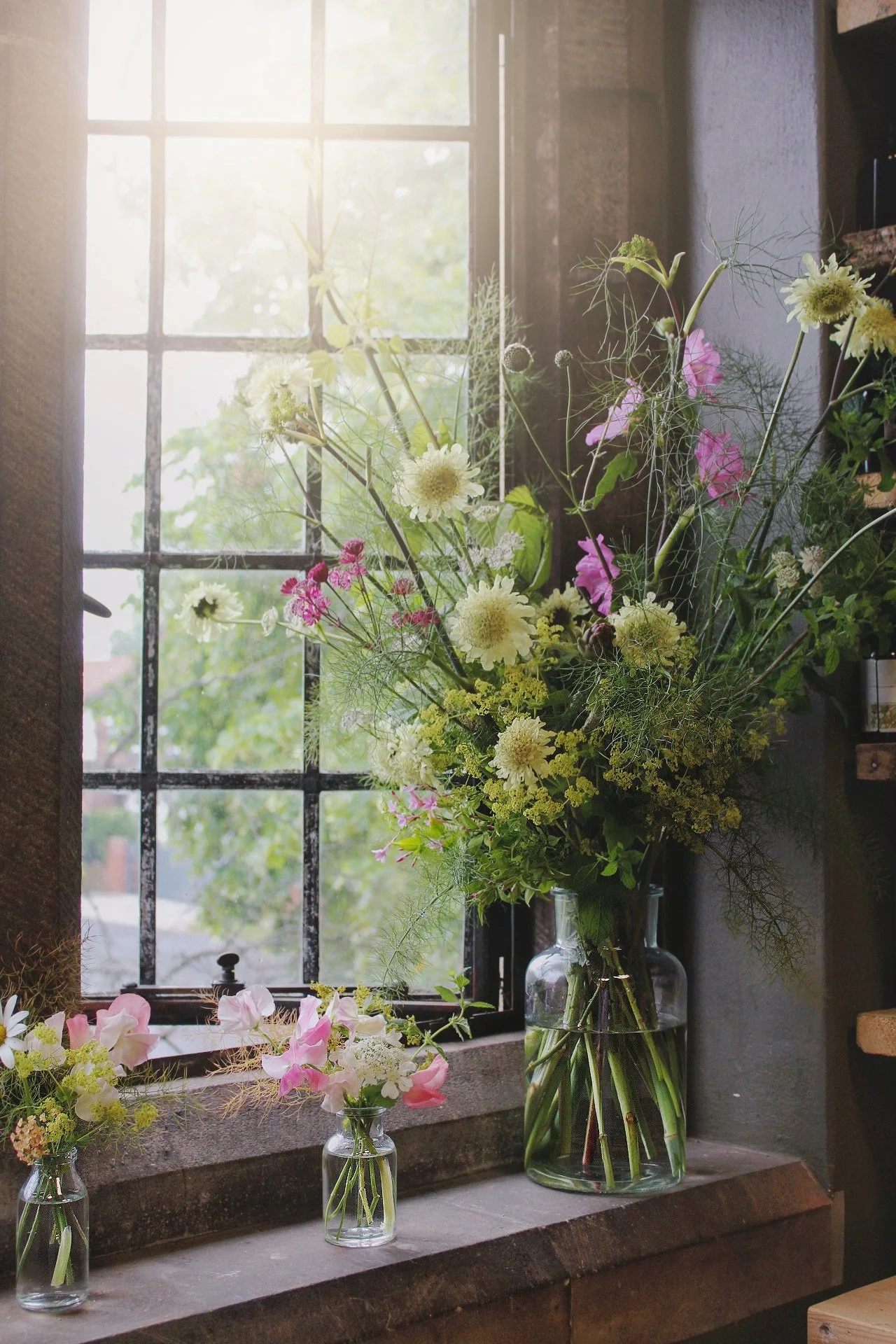 Signature bud vases arranged with tall seasonal flowers, airy stems and natural trailing foliage.