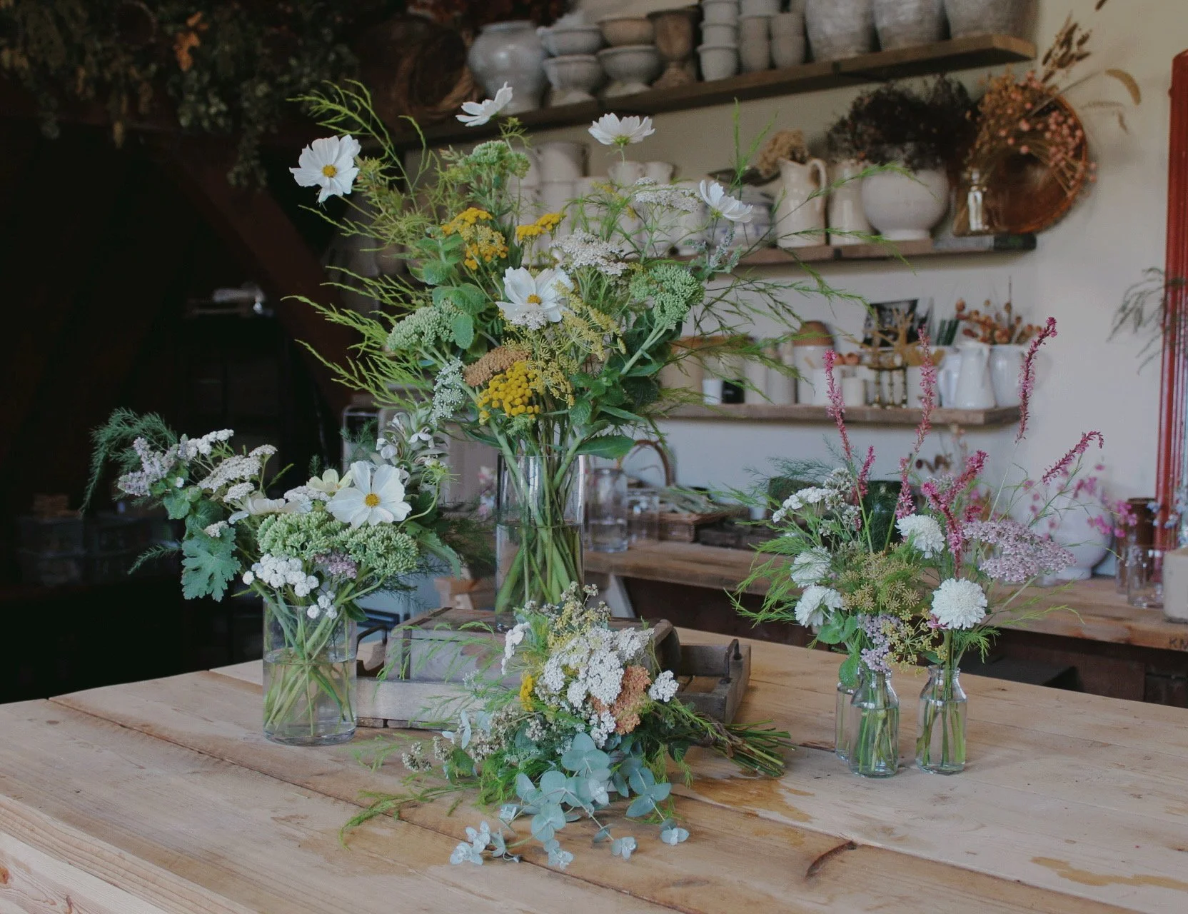 The Edit wedding flowers arranged in glass vases, featuring seasonal white, yellow and soft pink flowers with airy green foliage.