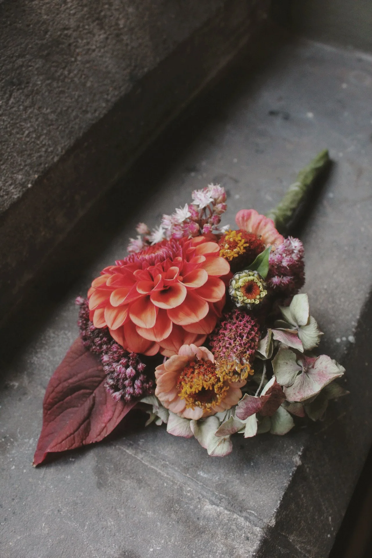 A ladies corsage pin, bouquet of various colourful flowers resting on a dark, textured concrete surface.
