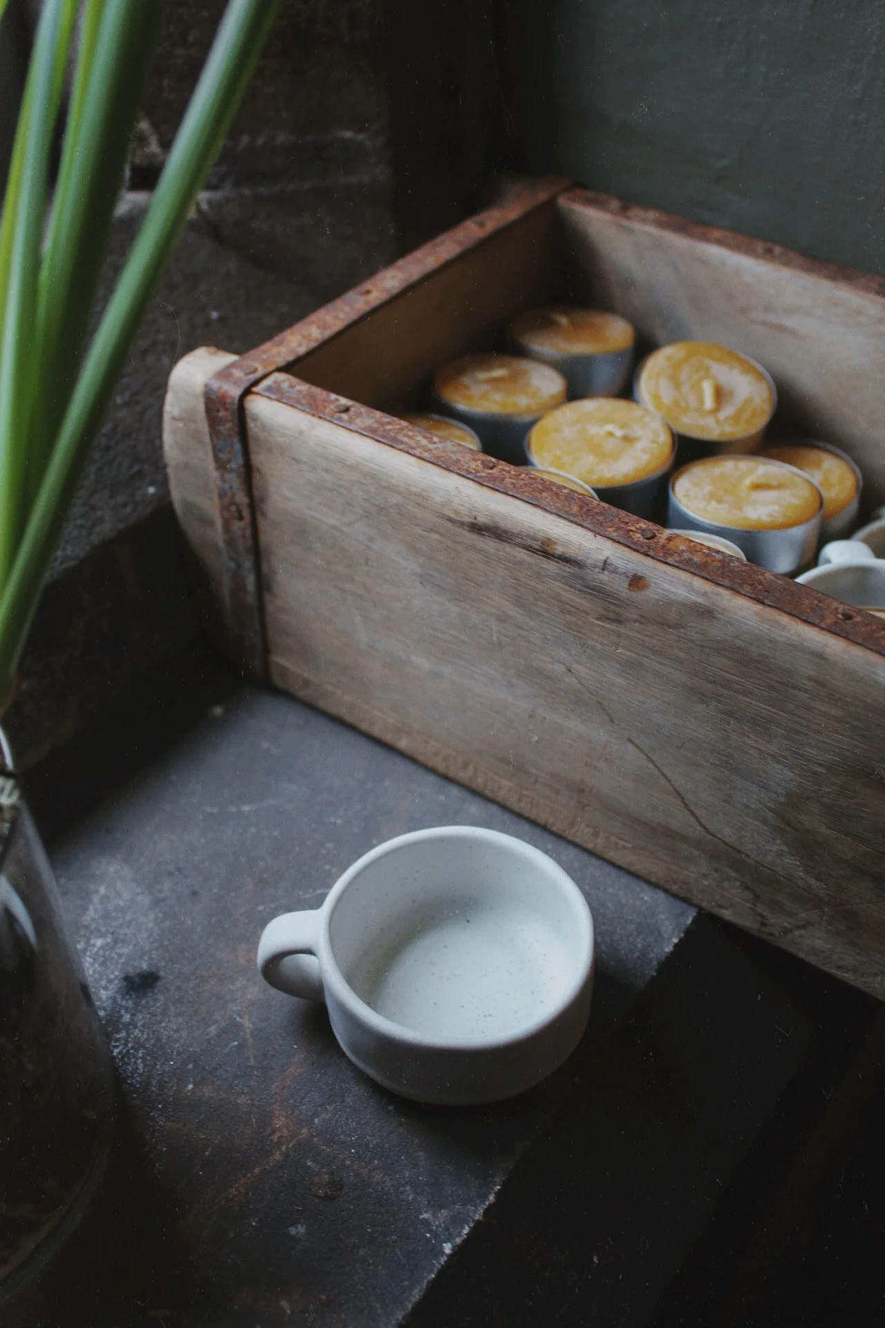 Small white ceramic candle dish with a beeswax tea light beside daffodils and candles.