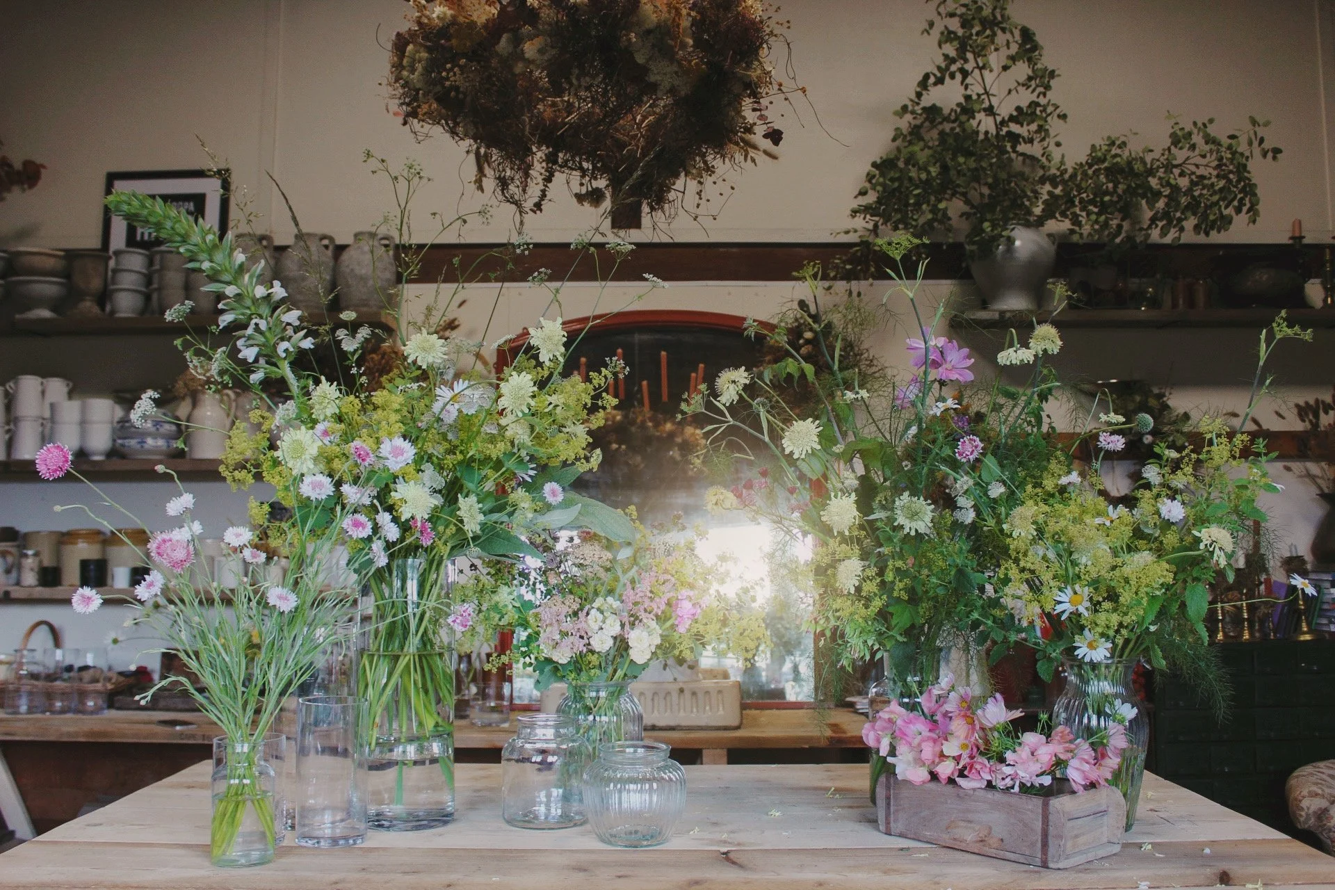 The Signature wedding flowers from The Wild Potager Co, showing abundant seasonal arrangements in glass vases, with natural, garden-grown movement and a mix of soft pink, white, yellow and green flowers.