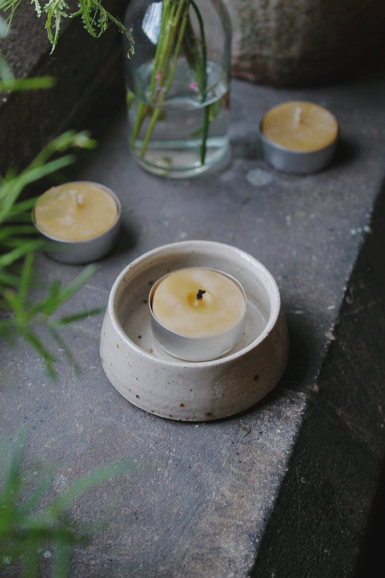 Speckled stone tea light holder with a lit candle beside a small glass vase of greenery.