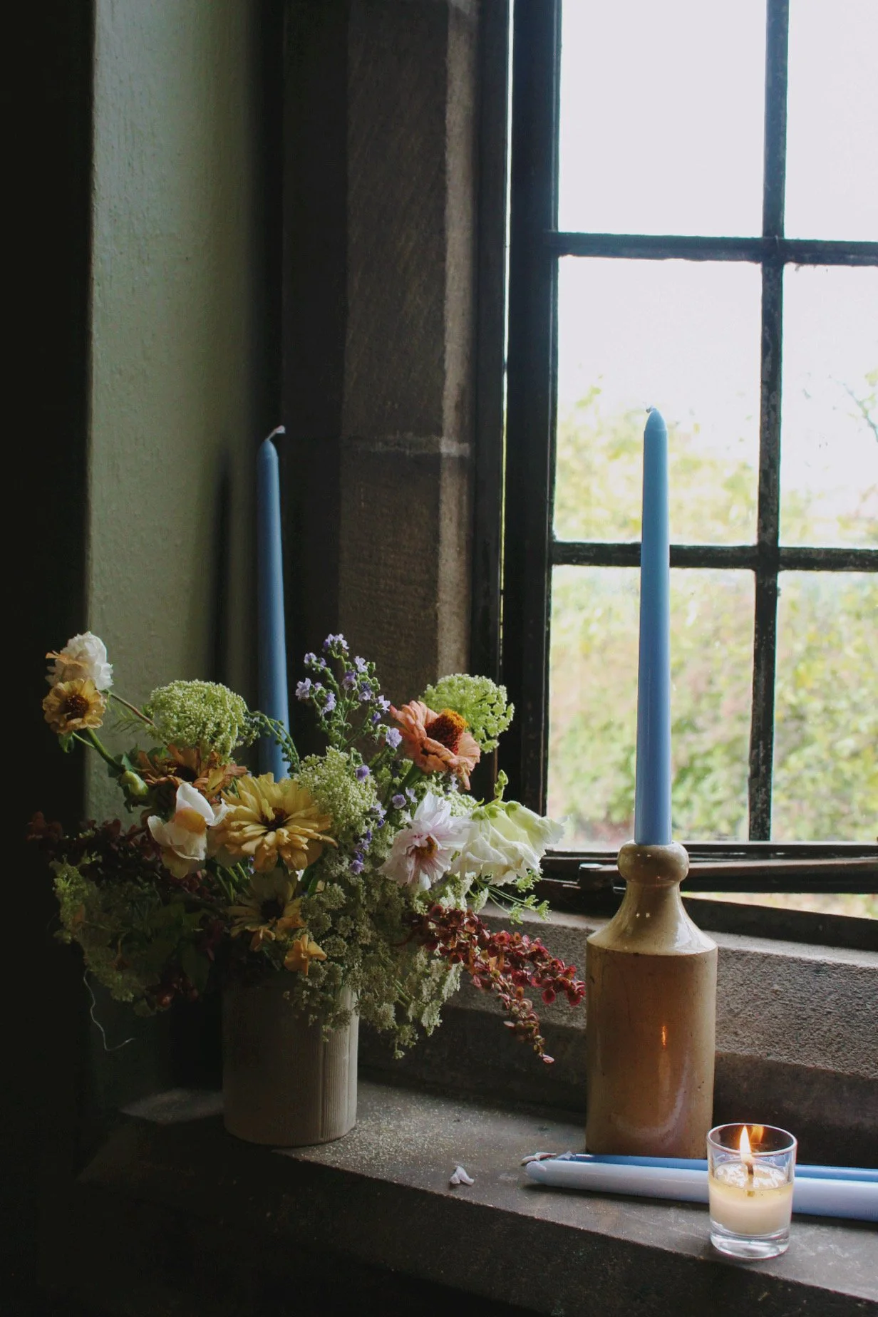 A flower arrangement and candles beside the old window in The Wild Potager Co studio.
