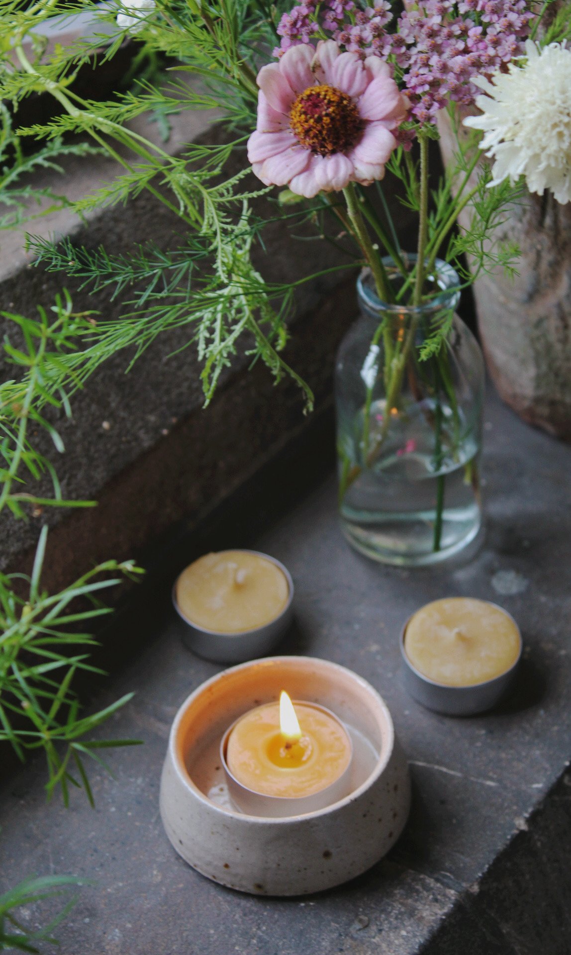 Speckled stone tea light holder with a lit candle beside a small glass vase of greenery.