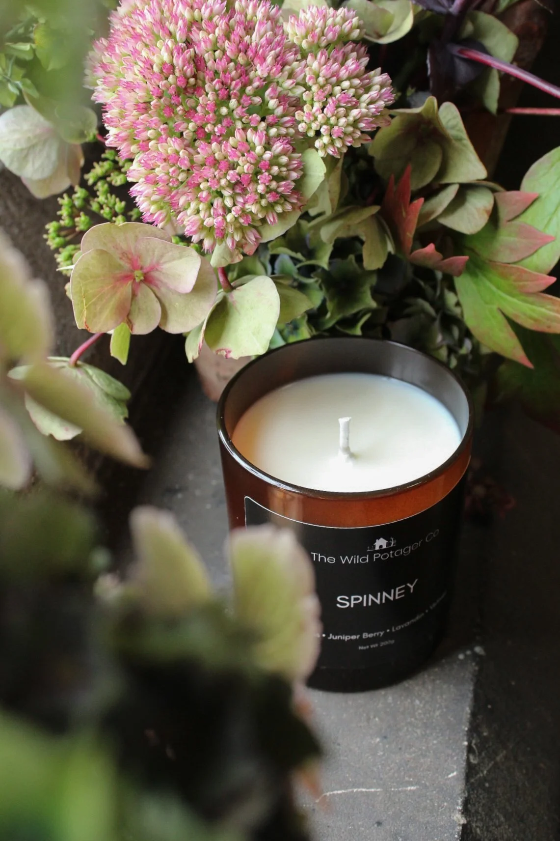 Spinney soy wax candle surrounded by seasonal flowers and foliage