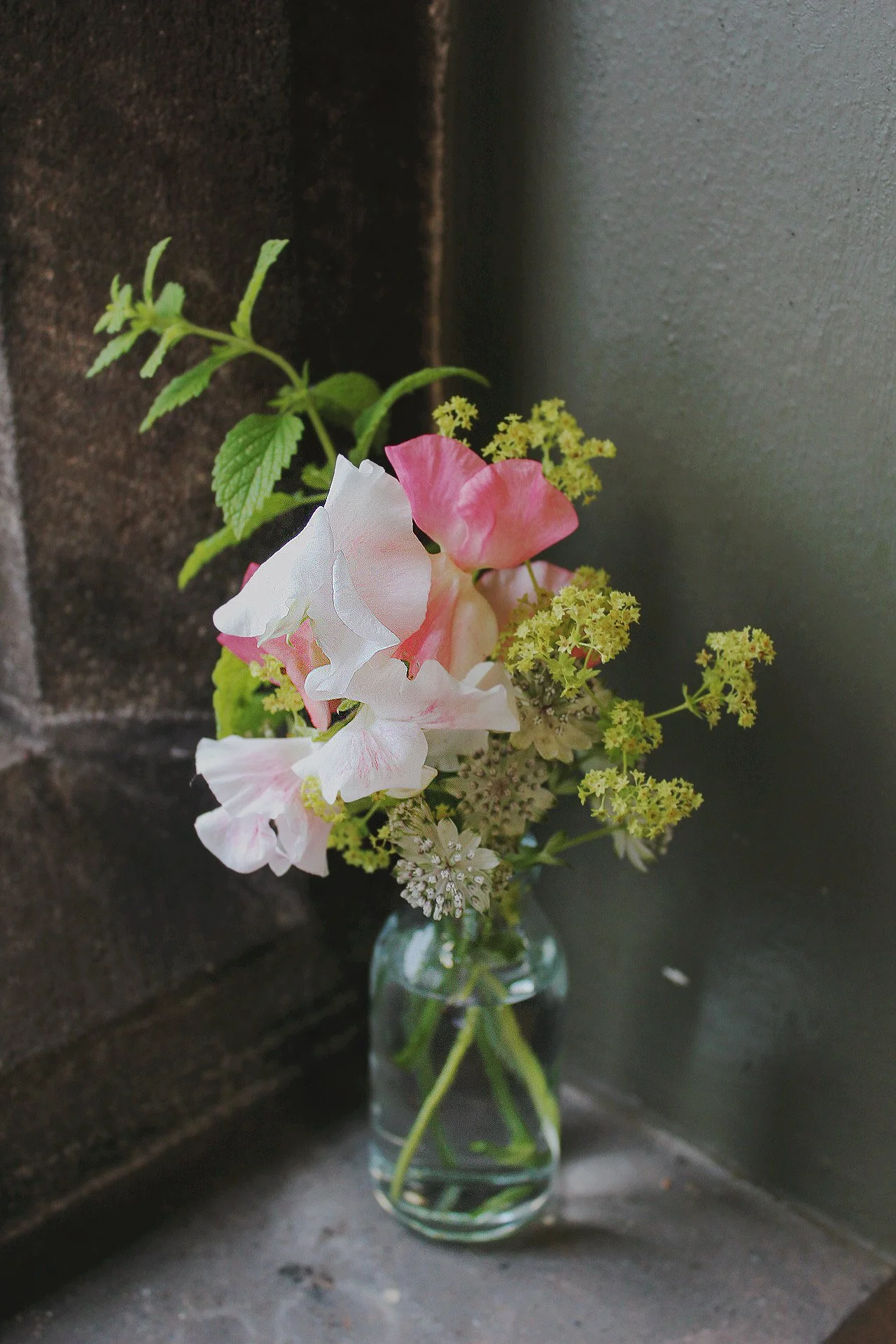 Small glass bud vase filled with delicate seasonal wedding flowers on a stone windowsill.