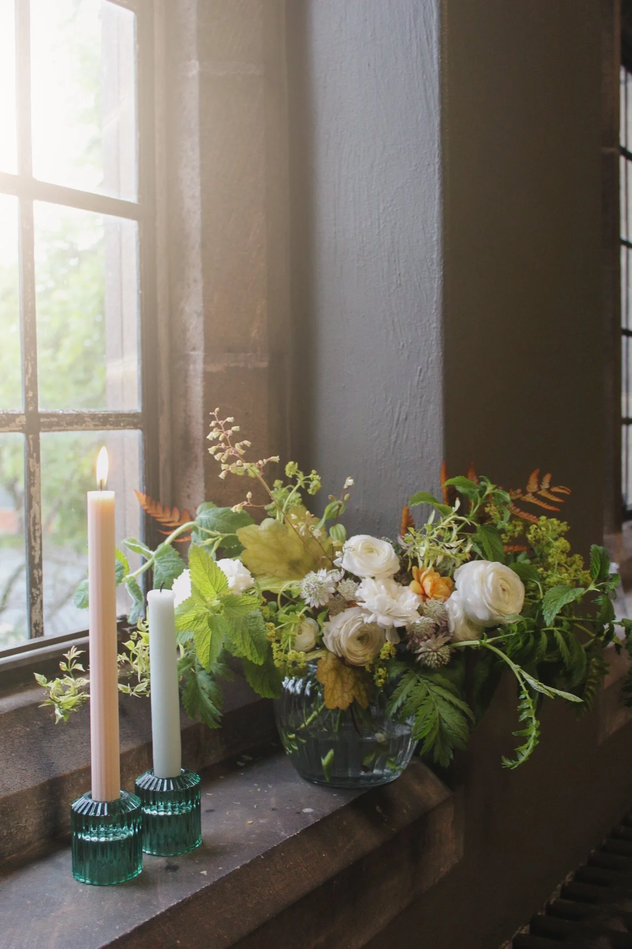 Ribbed glass classic centrepiece filled with abundant seasonal flowers and foliage, styled with taper candles on a wedding table.