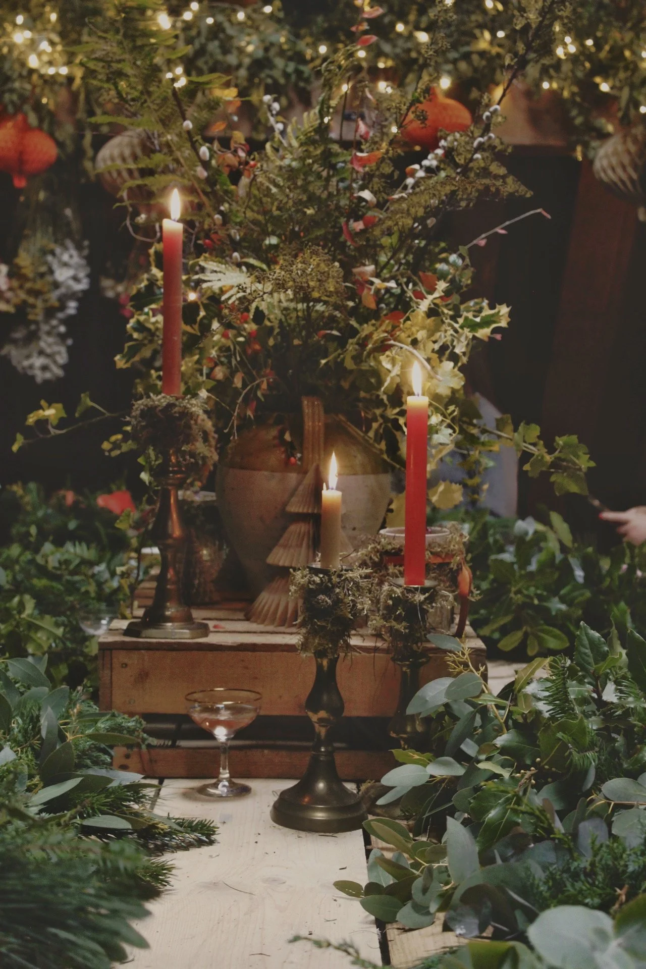 Decorative arrangement with candles, greenery, and lights, possibly for a holiday or special event.