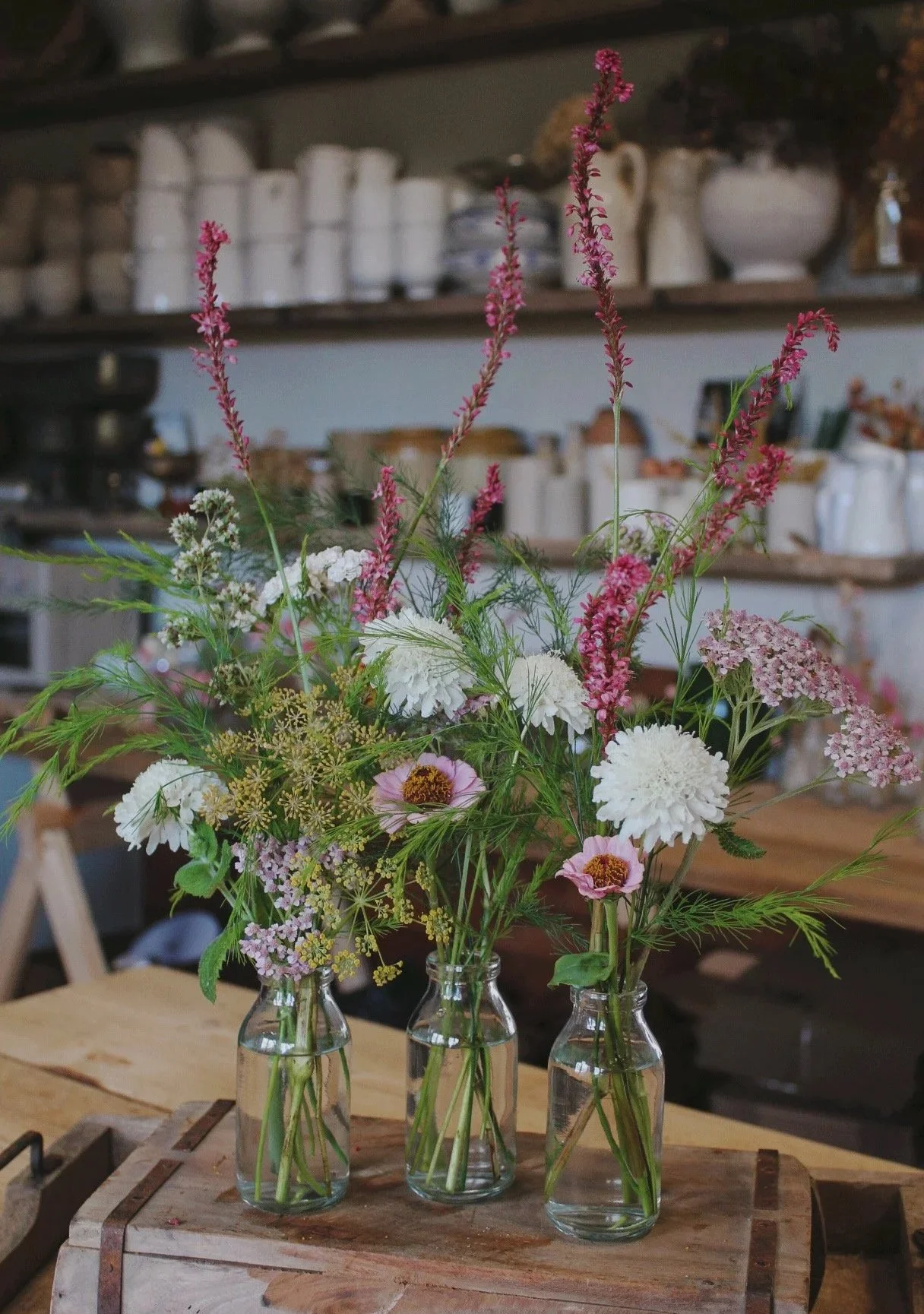 Edit bud vases filled with fresh seasonal flowers, soft foliage and varied flowering stems for a relaxed wedding display.